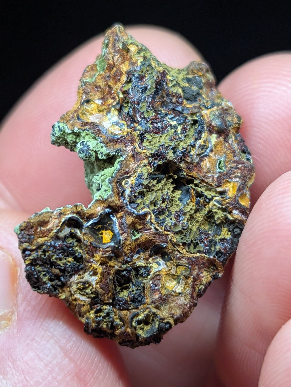 A rugged, irregularly shaped mineral specimen with a textured surface displaying patches of vibrant green, earthy brown, and hints of yellowish-orange.