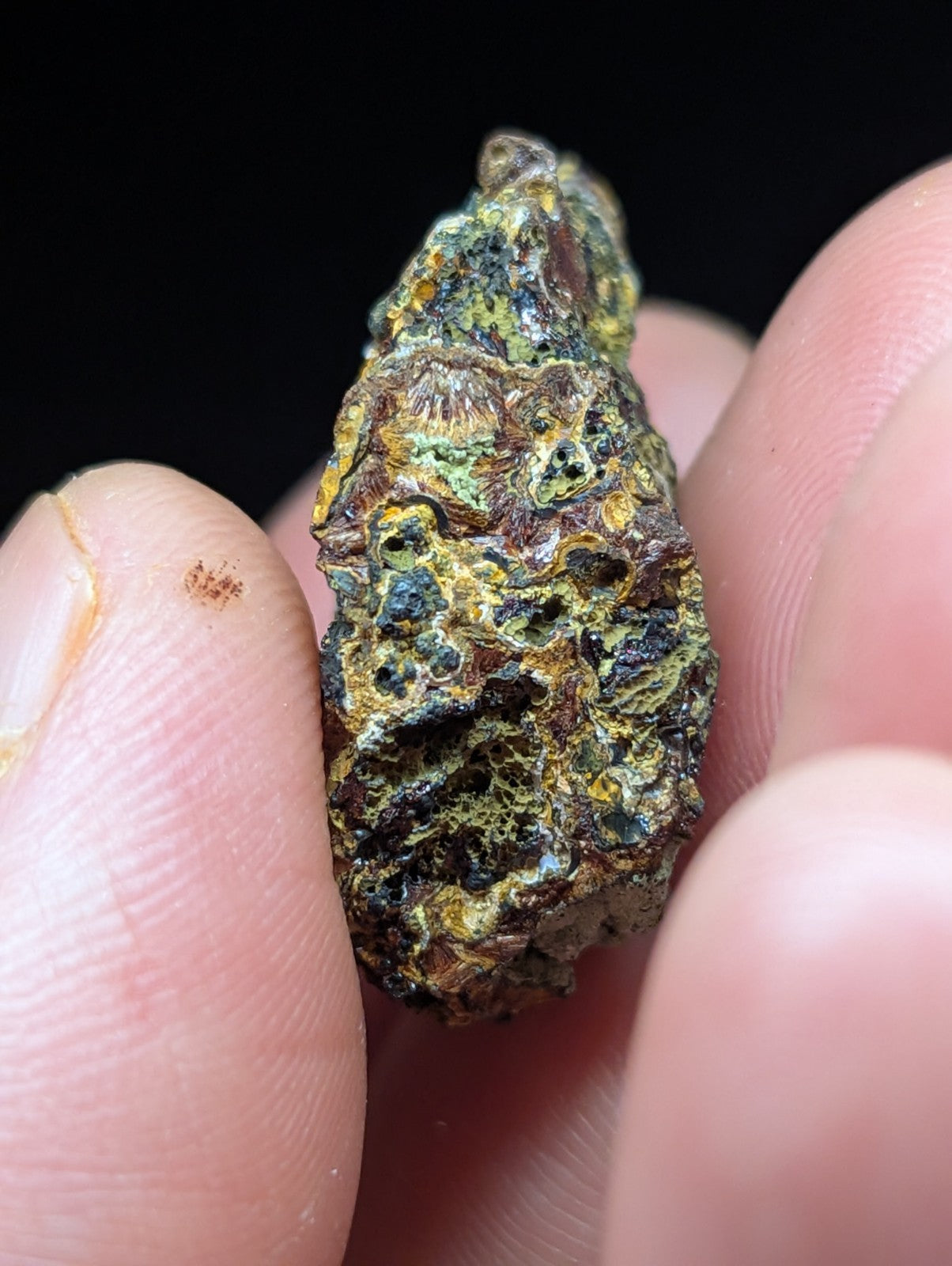 A rough, irregularly shaped mineral specimen with a mottled surface of green, yellow, and dark brown hues.