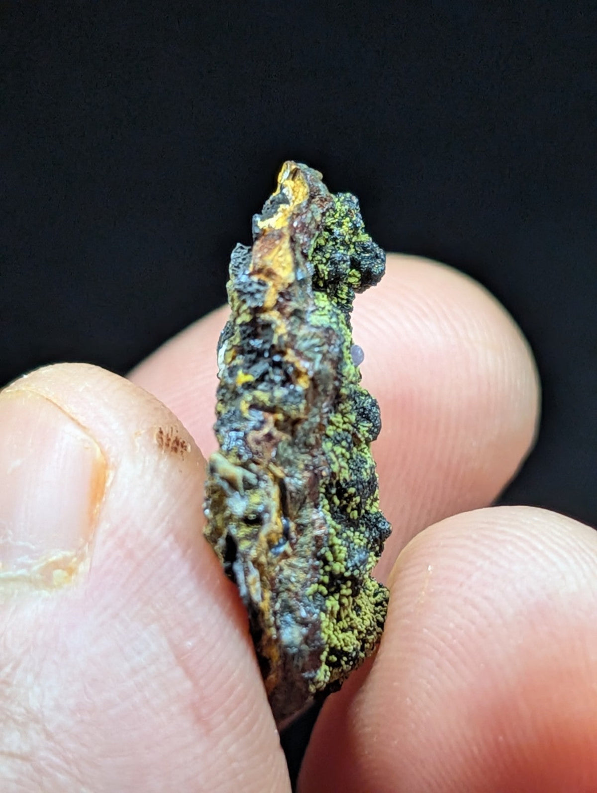 A rugged, irregularly shaped mineral specimen with a textured surface featuring patches of greenish moss-like growth and dark brown to black areas.