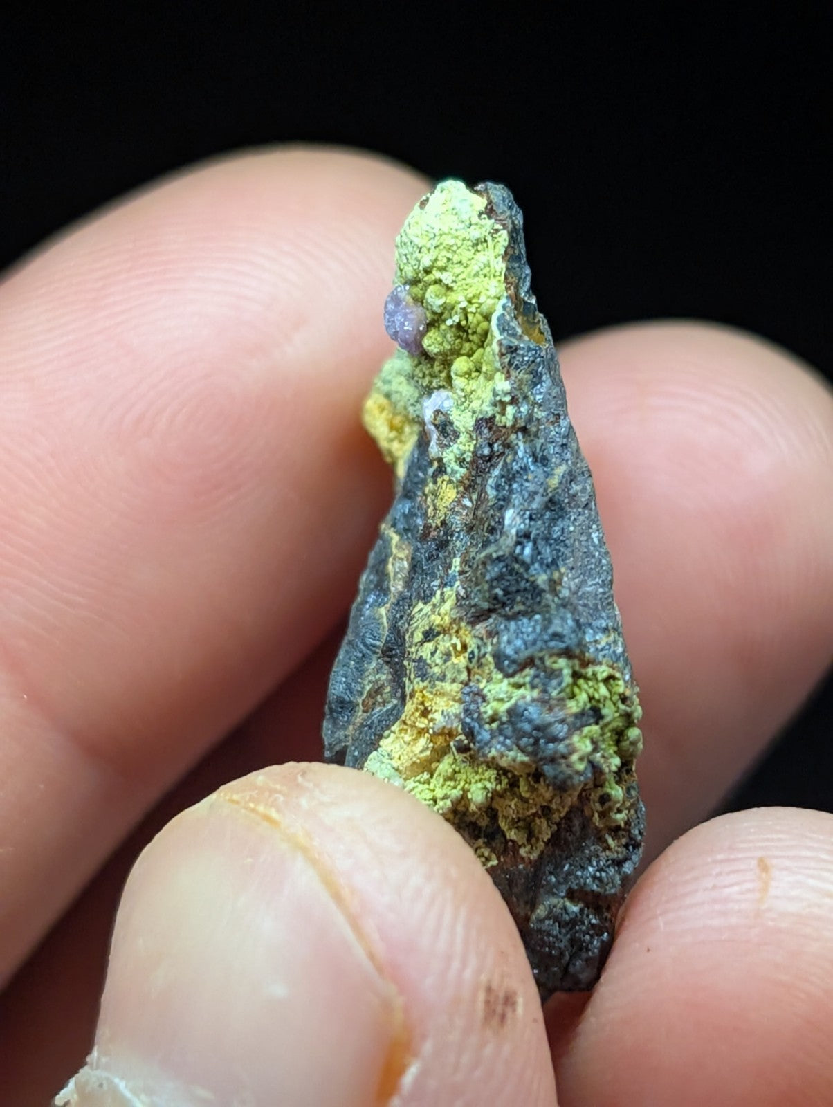 A rugged, dark gray mineral specimen with vibrant green and yellow patina patches.