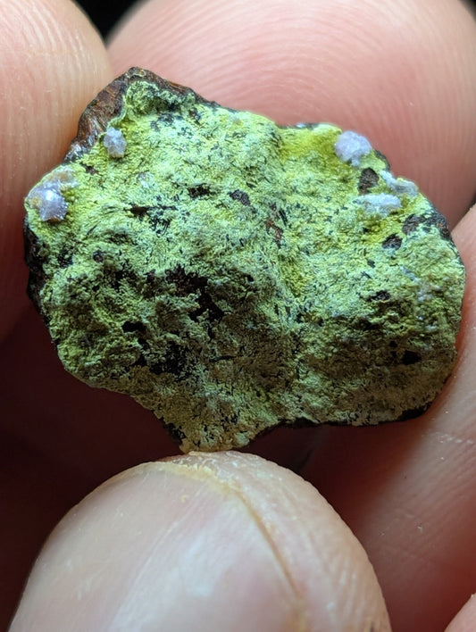 A rough, irregularly shaped mineral specimen with a vibrant green patina and small white crystalline formations.