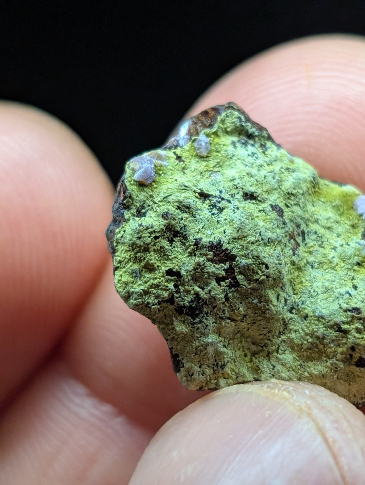 A rough, irregularly shaped mineral specimen with a vibrant green patina and scattered dark patches.