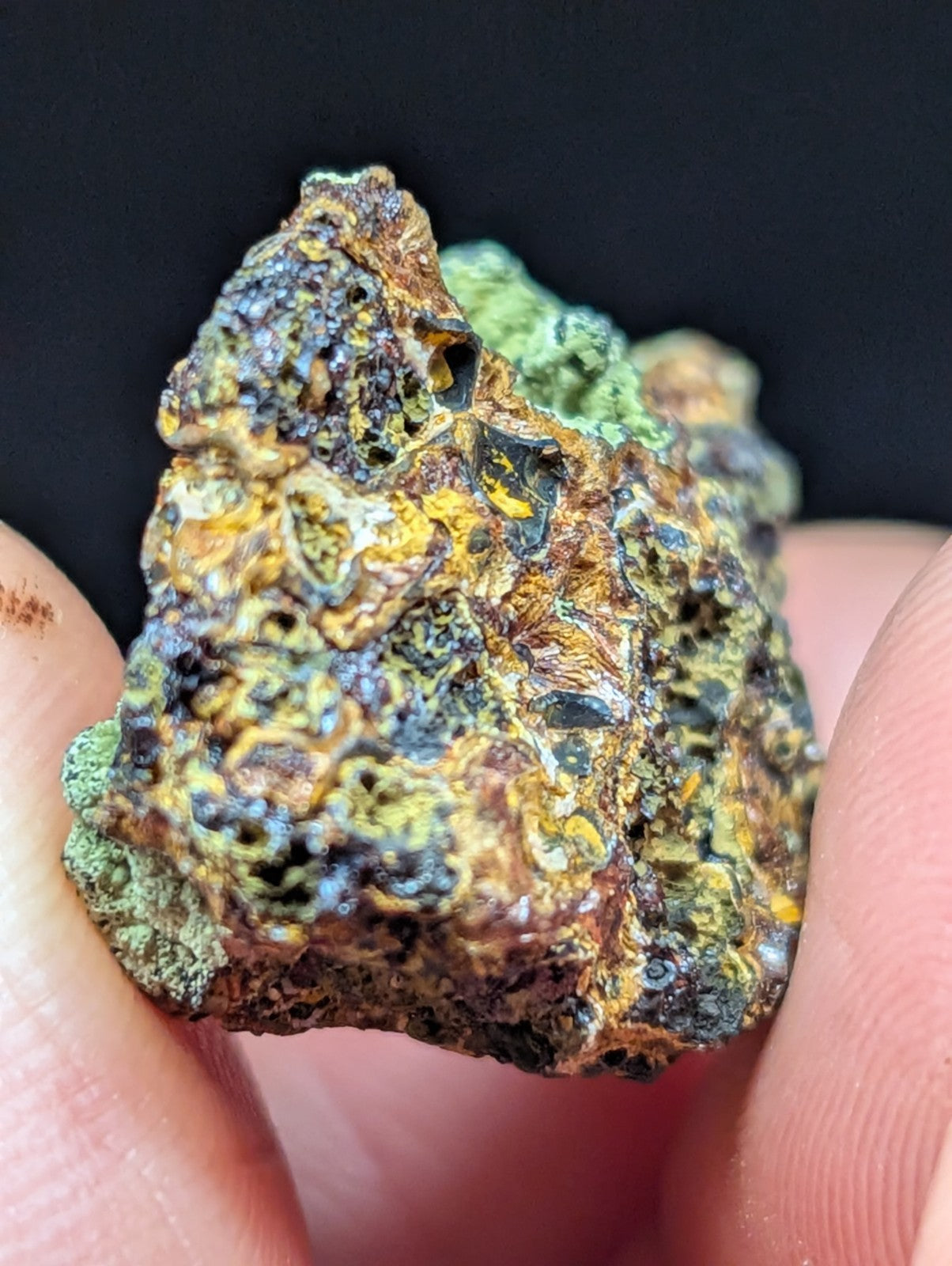 A rugged, irregularly shaped mineral specimen with a textured surface displaying patches of green, yellow, and dark brown hues.