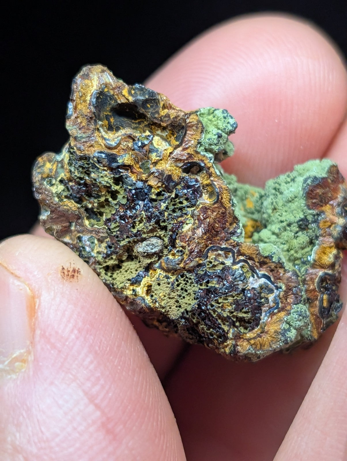 A rugged, multicolored mineral specimen with patches of green moss-like growth and intricate patterns in brown, yellow, and dark blue.