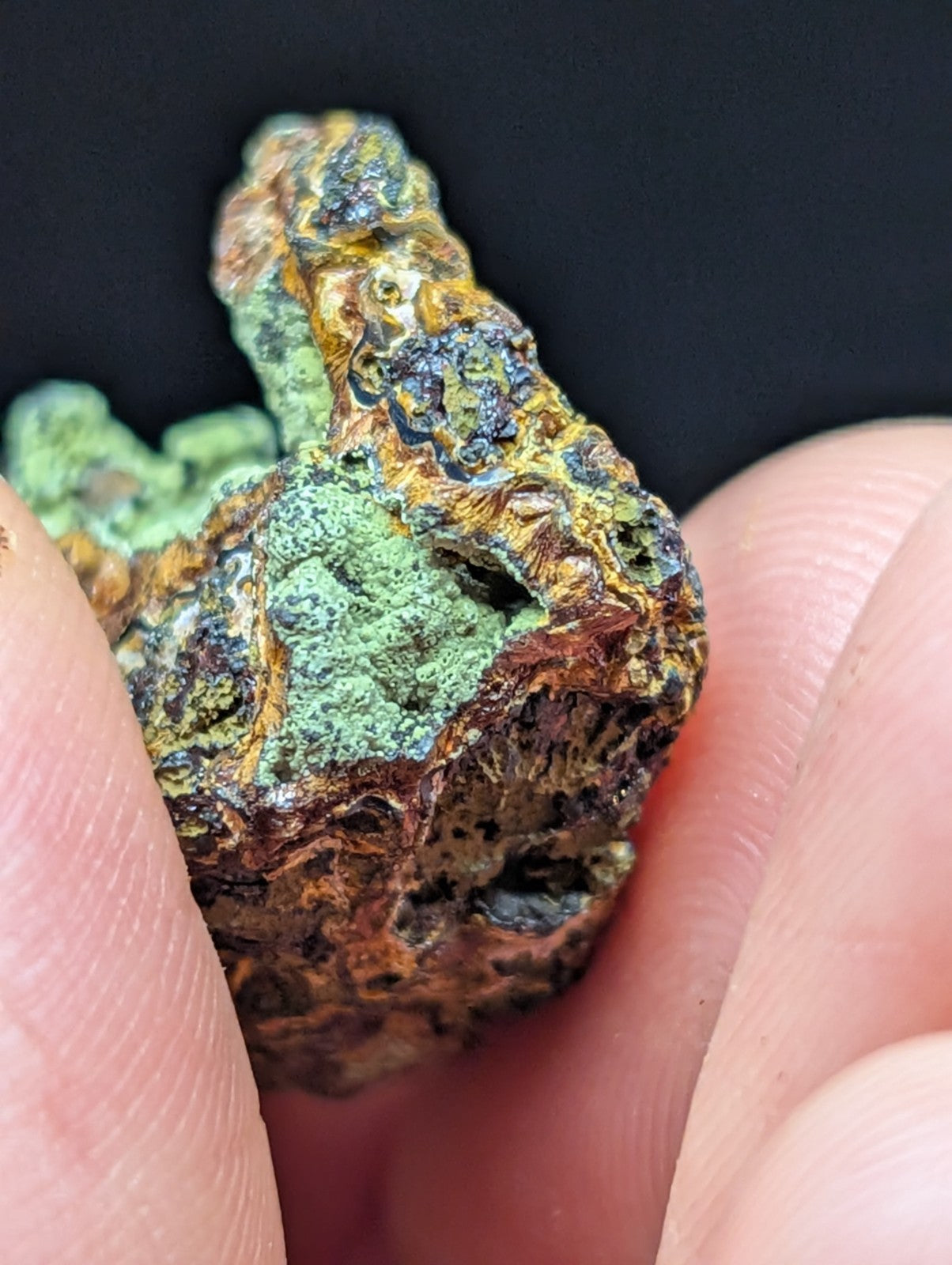 A rugged, irregularly shaped mineral specimen with patches of vibrant green patina and areas of dark brown and orange oxidation.