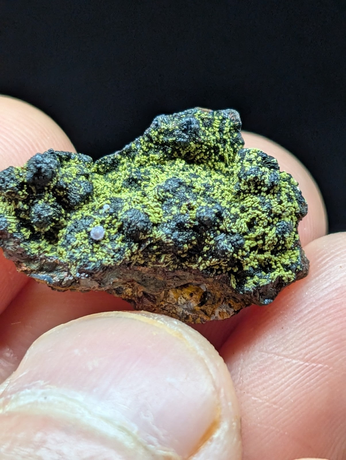 A rough, irregularly shaped mineral specimen featuring vibrant green and dark black patches with a textured surface.