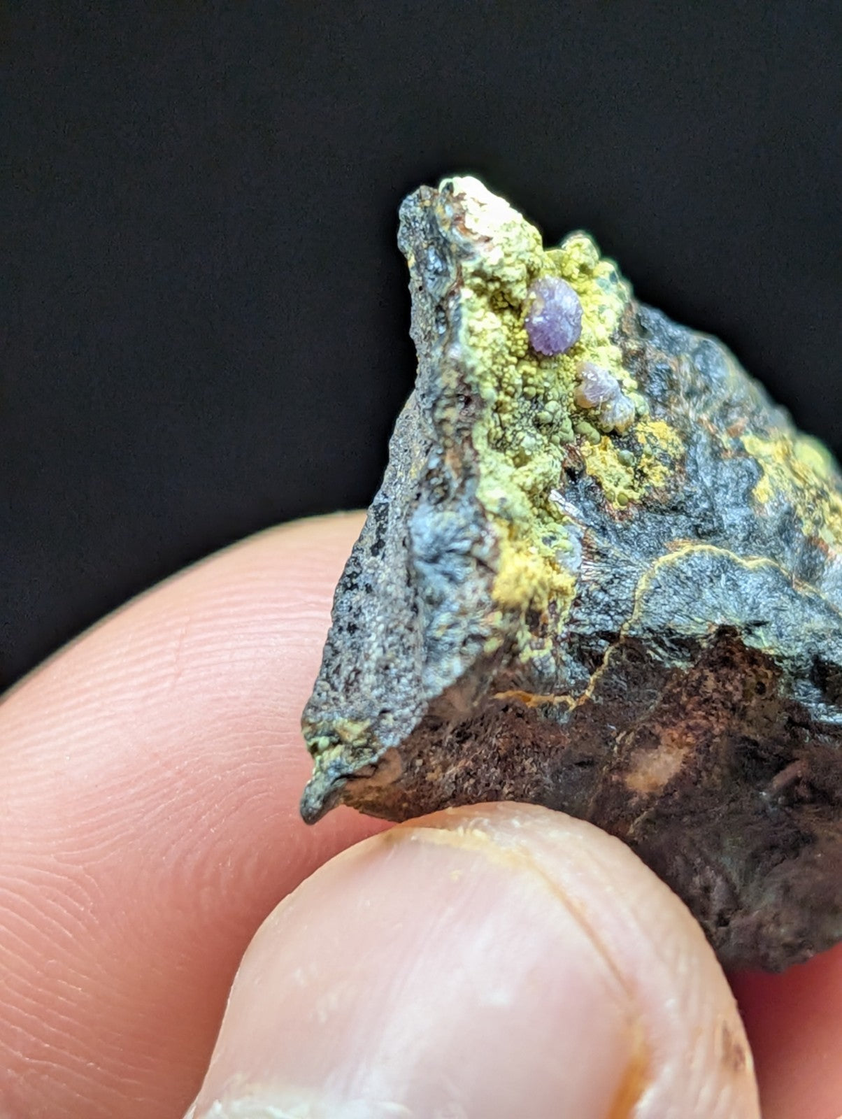 A rugged, dark mineral specimen with vibrant green and purple crystalline inclusions.
