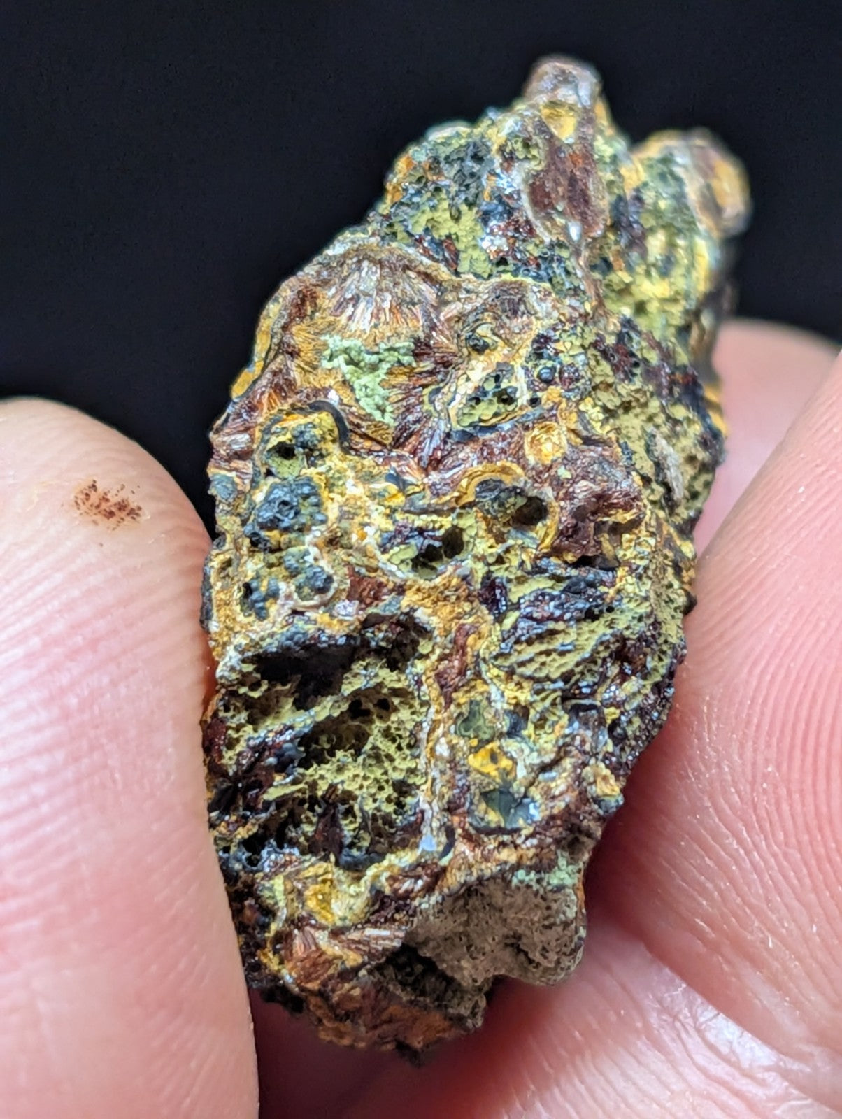 A rugged, irregularly shaped mineral specimen with a textured surface displaying patches of vibrant green and yellow hues interspersed with dark brown and black areas.