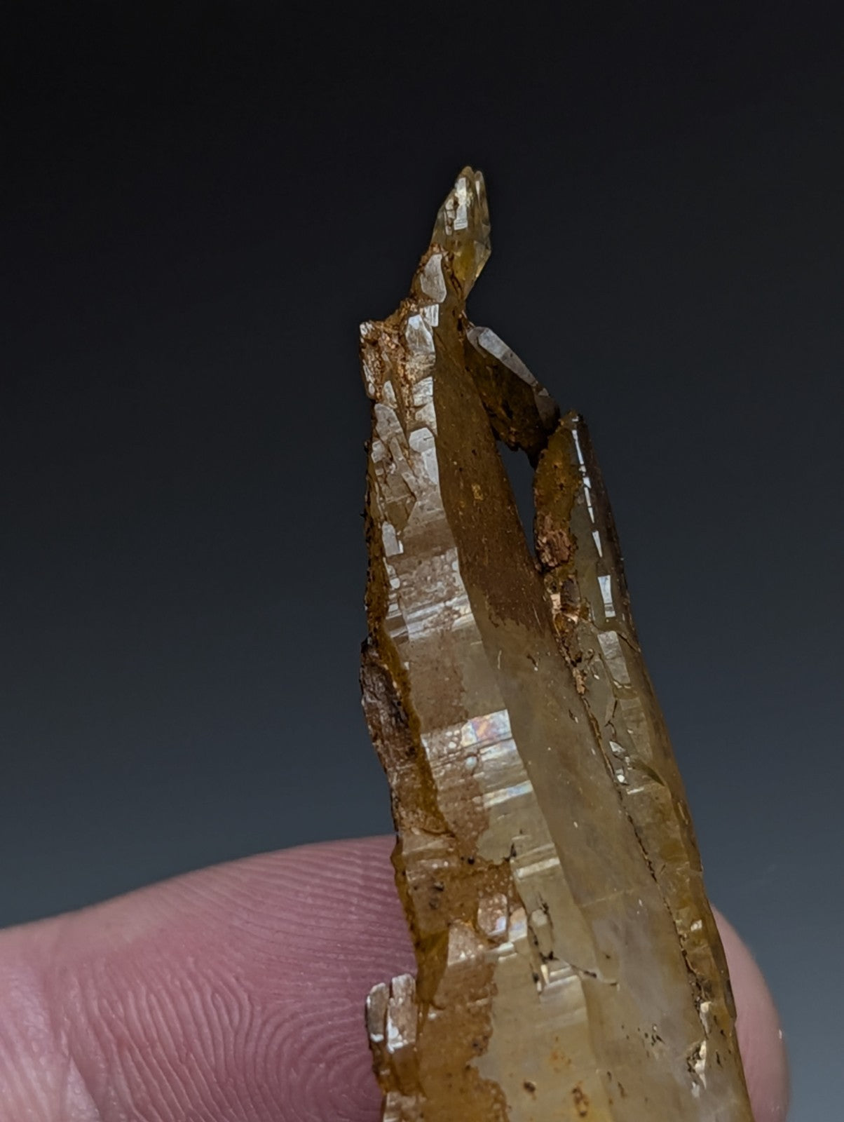 A translucent amber quartz crystal with striations and imperfections held between fingers from Garland County Arkansas