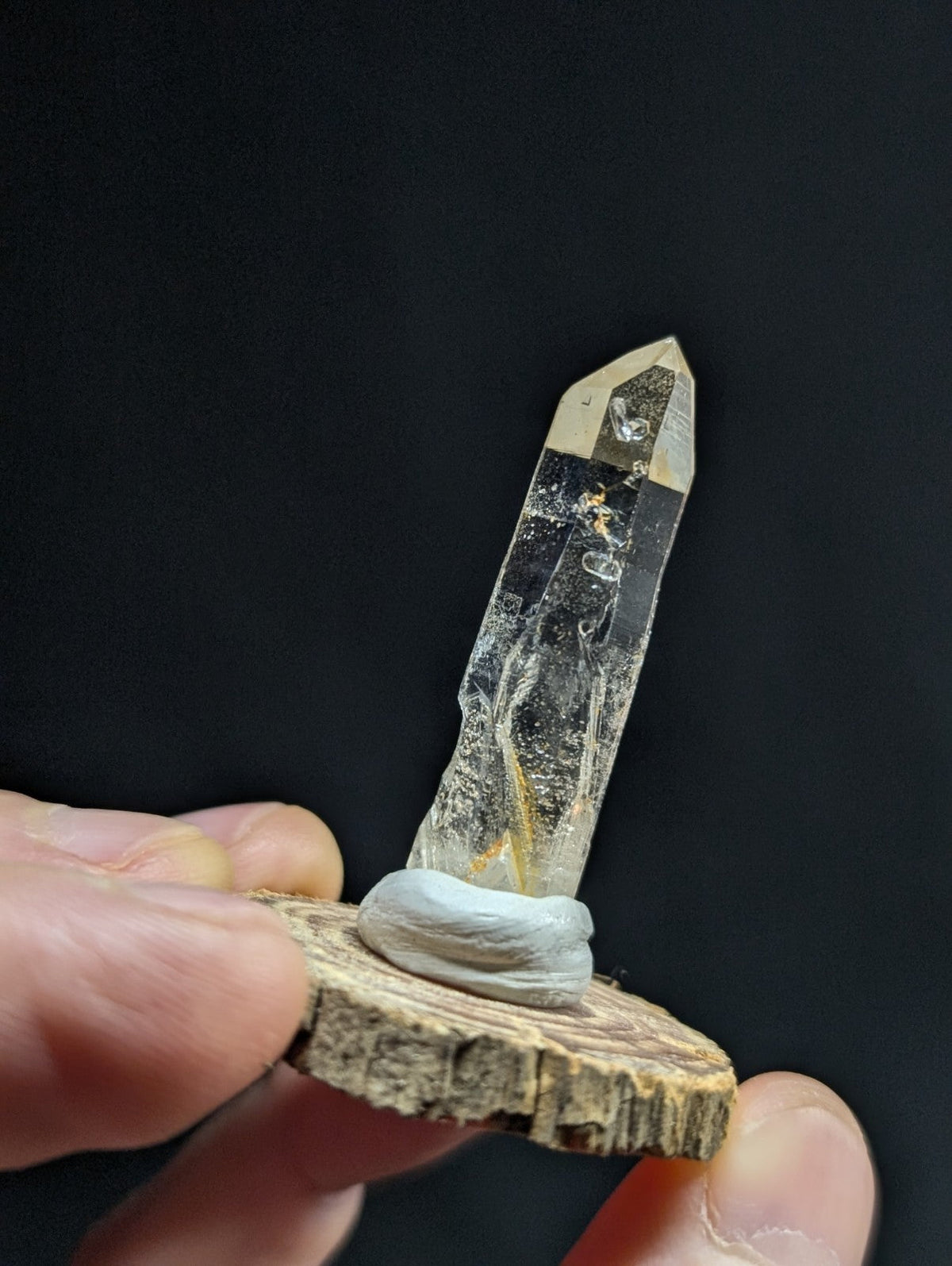 A clear quartz crystal with golden inclusions, mounted on a rustic wooden slice.
