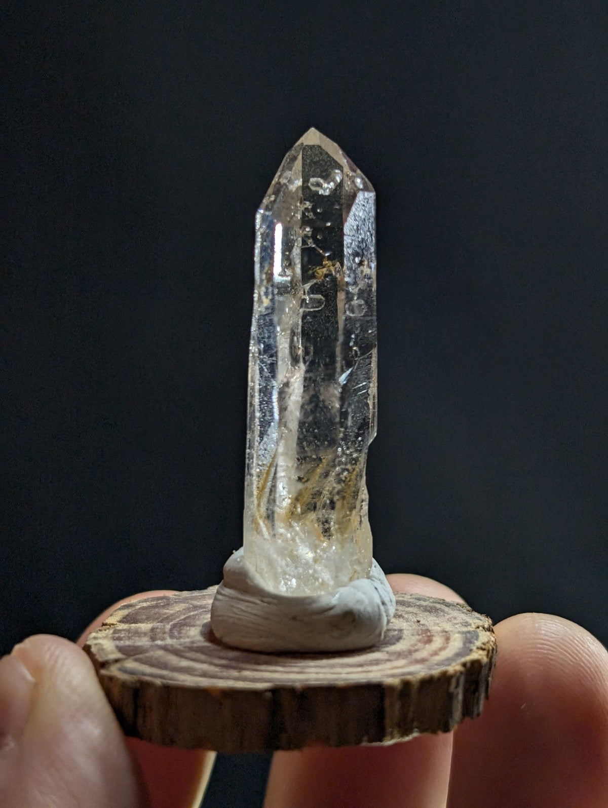 A clear quartz crystal with natural inclusions and a pointed tip, mounted on a rustic wooden slice base.