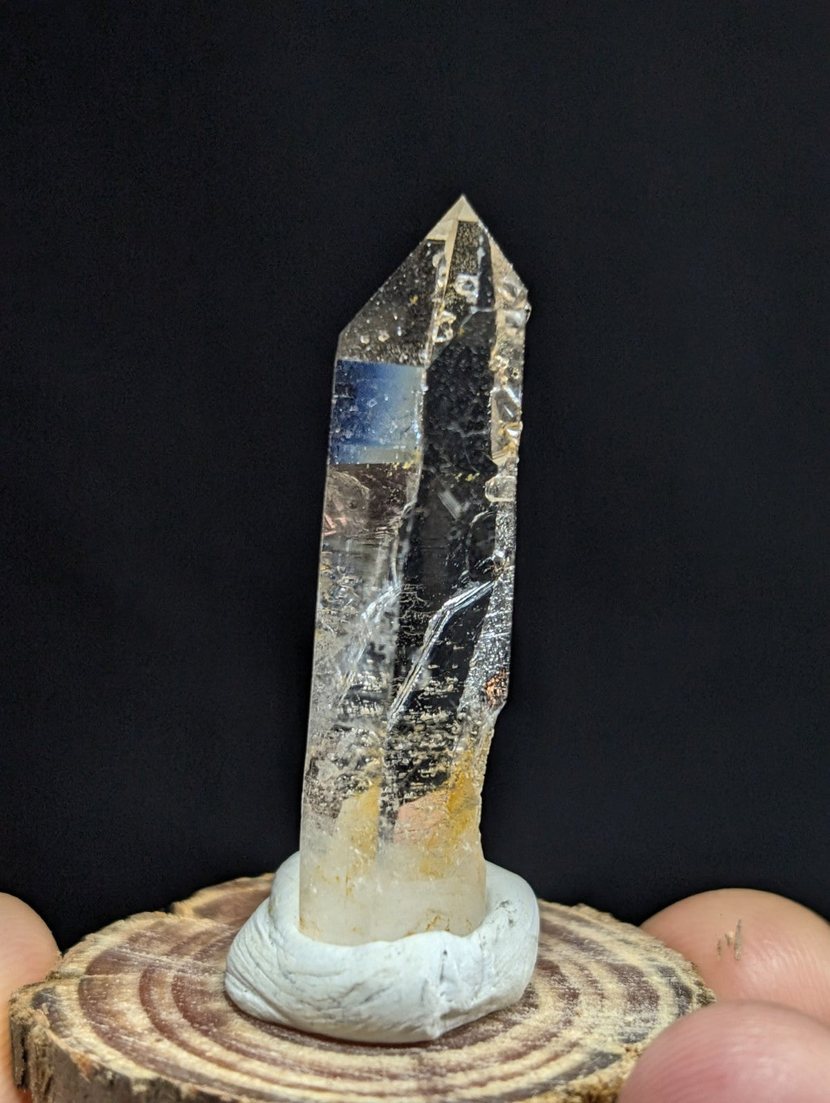 A clear quartz crystal with golden inclusions and a pointed tip, mounted on a white ceramic base.