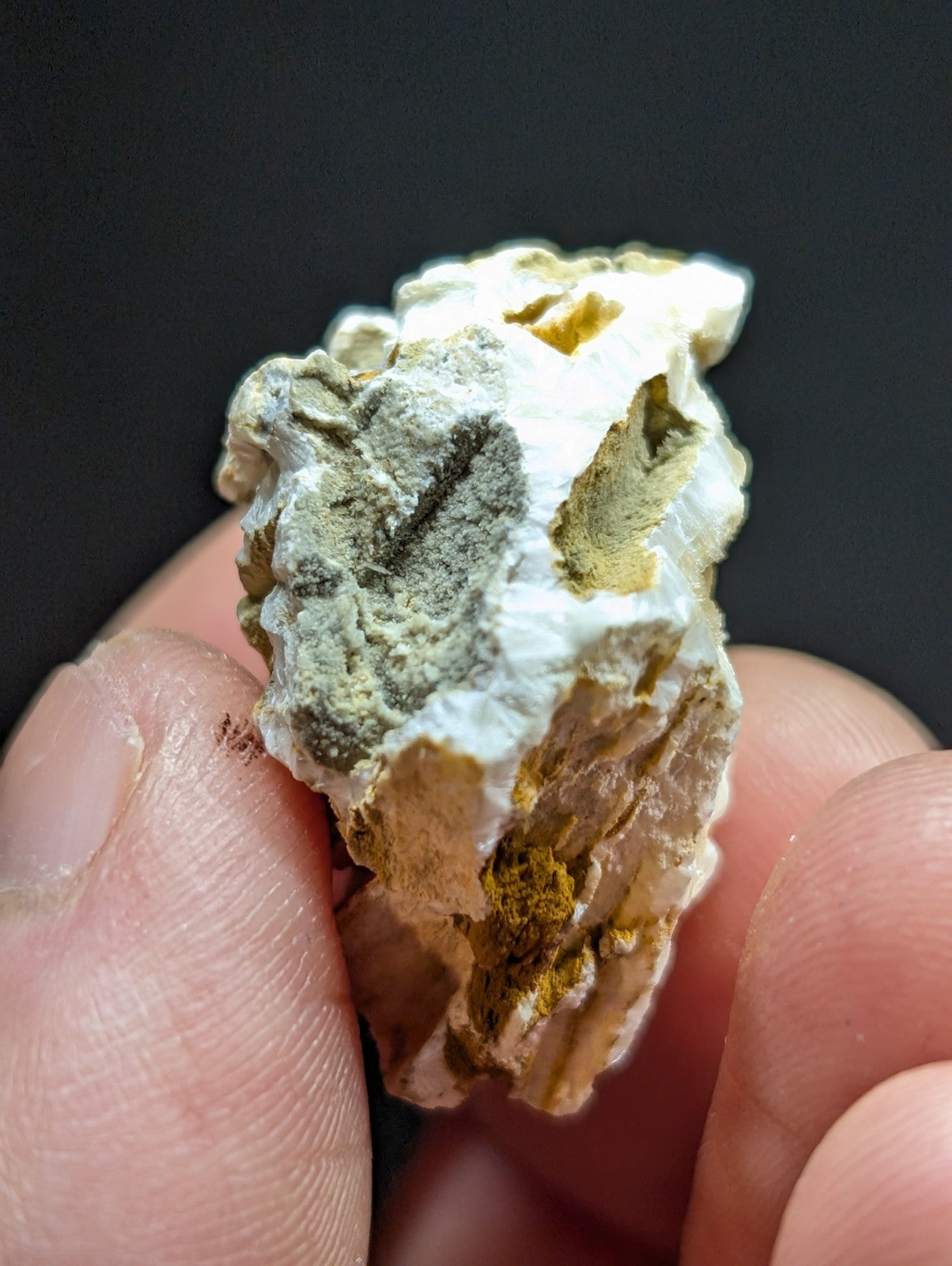 A rough, irregularly shaped mineral specimen with a mix of white, grayish-green, and golden-yellow hues.