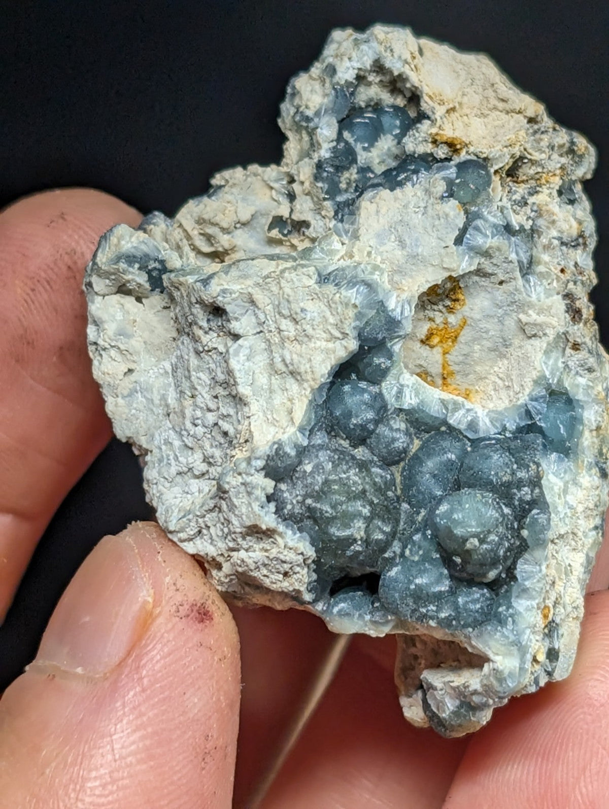 A rough, irregularly shaped mineral specimen featuring clusters of translucent blue crystals embedded in a pale gray matrix with subtle yellowish streaks.
