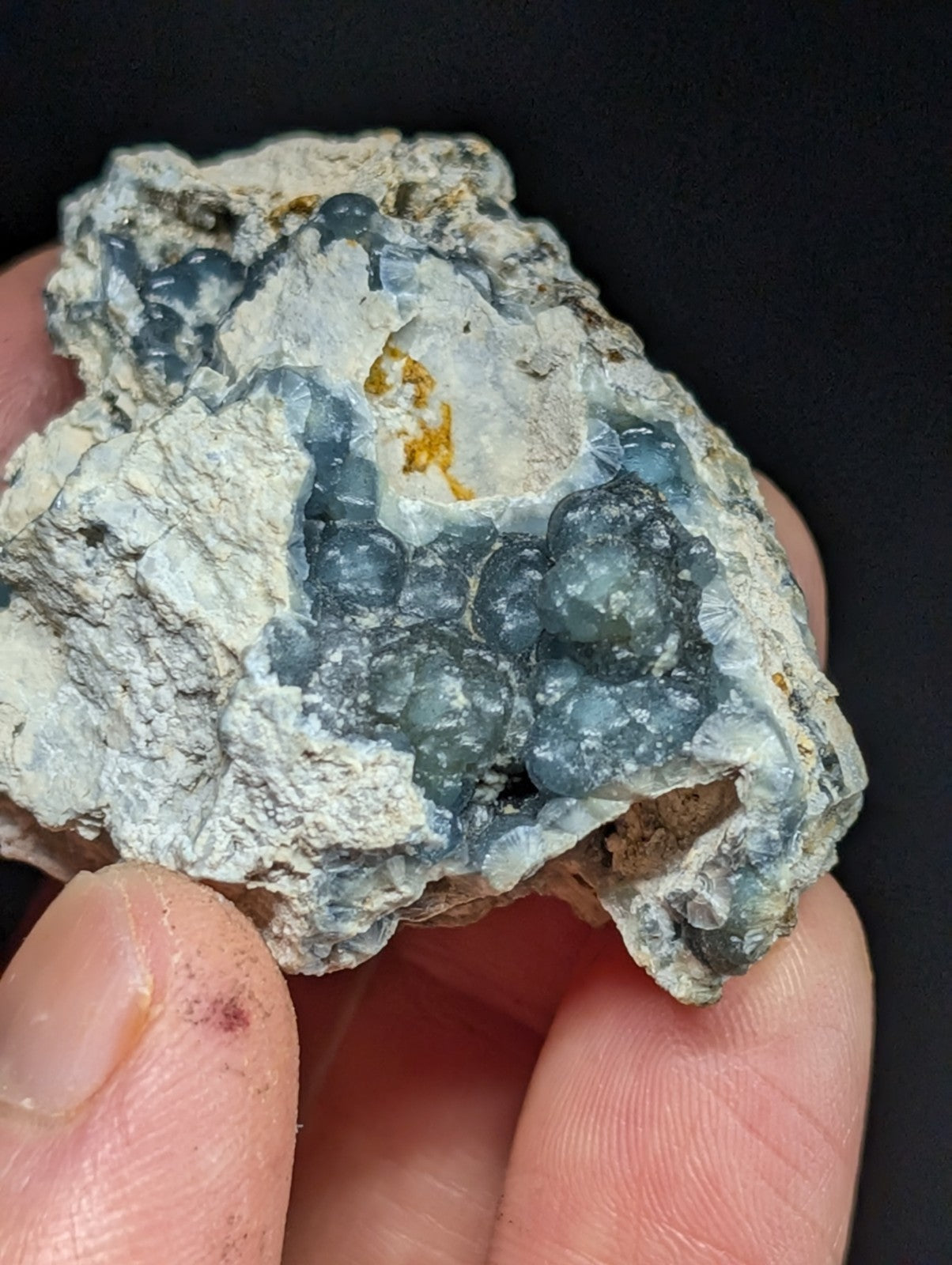 A hand holds a rough, irregularly shaped geode with translucent blue and gray crystalline formations embedded in a white matrix.