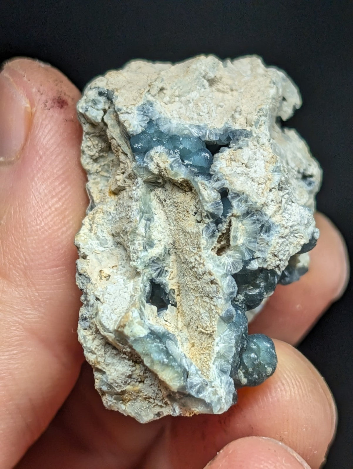 A rough, irregularly shaped mineral specimen with a pale gray matrix and clusters of translucent blue-green crystals.