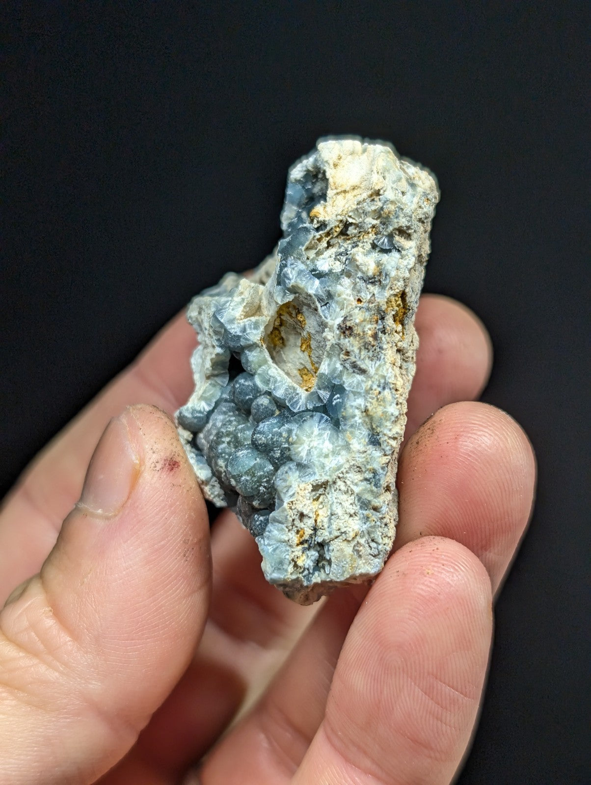 A rough, irregularly shaped blue-gray mineral specimen with crystalline formations and patches of yellowish material.