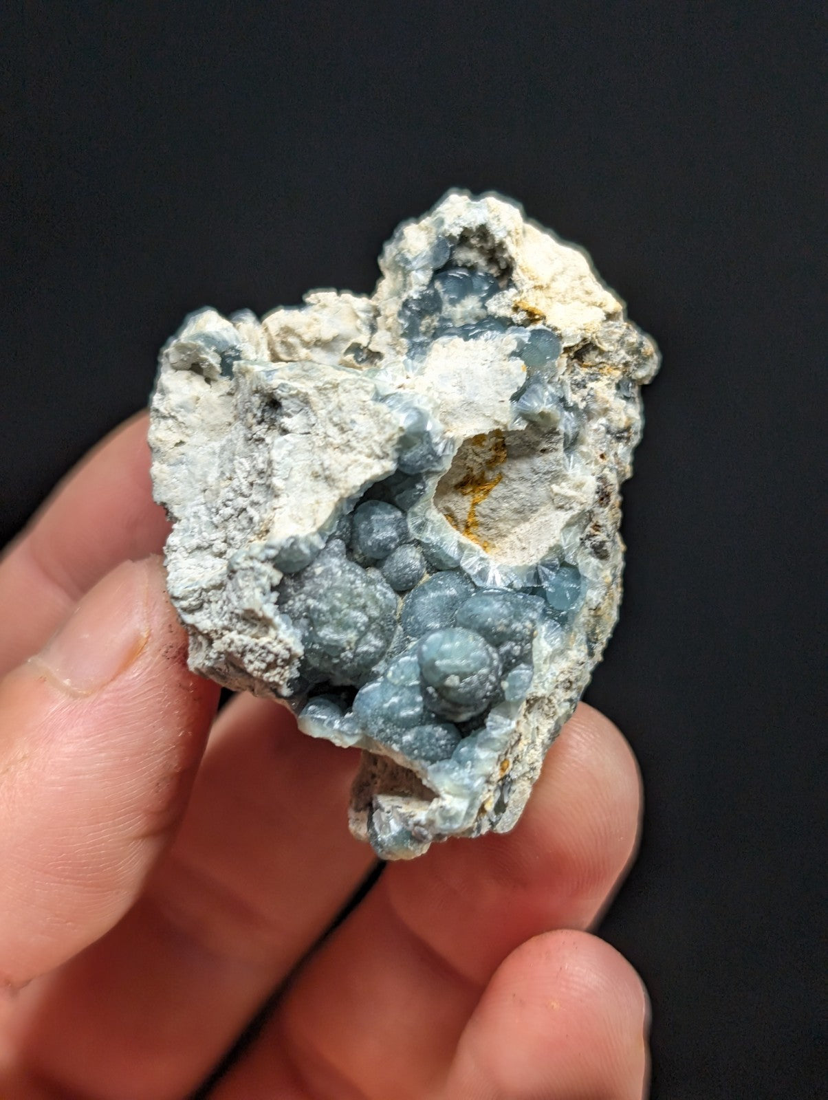 A hand holds a rough, irregularly shaped geode with a striking blue-gray crystalline interior and white, porous matrix.