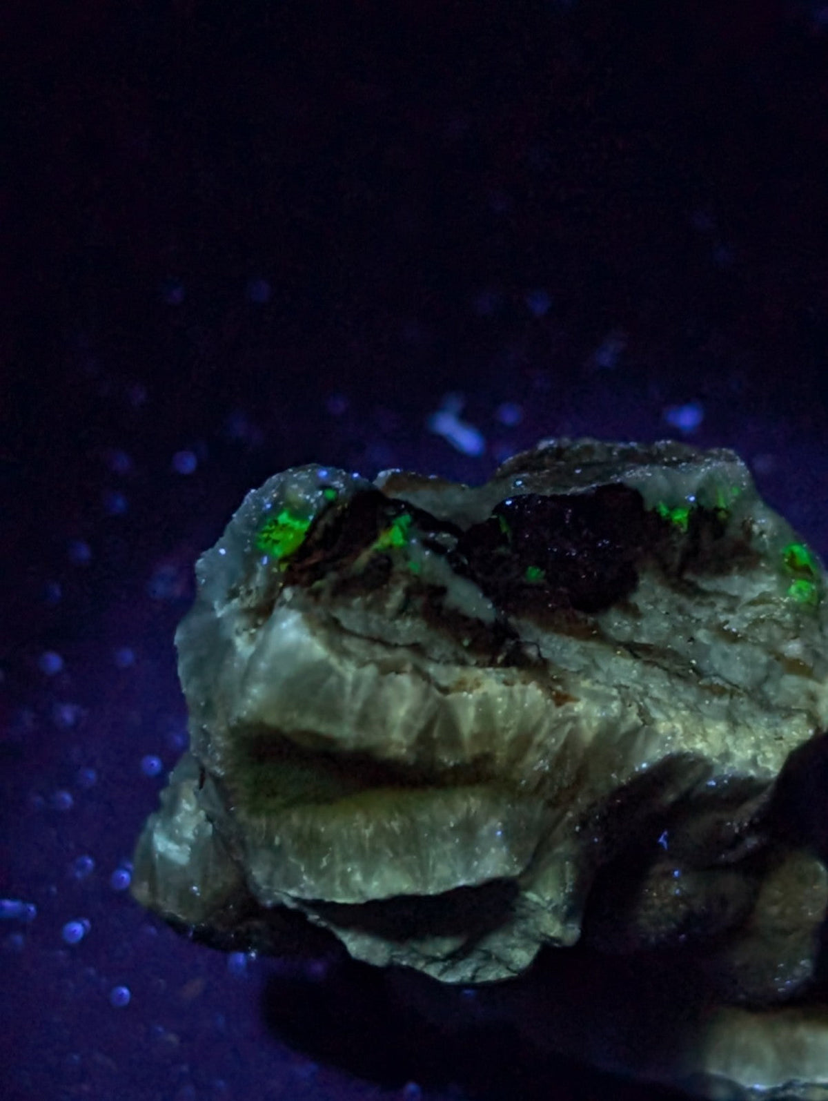 A rugged, irregularly shaped rock with a rough, textured surface and patches of glowing green mineral inclusions.