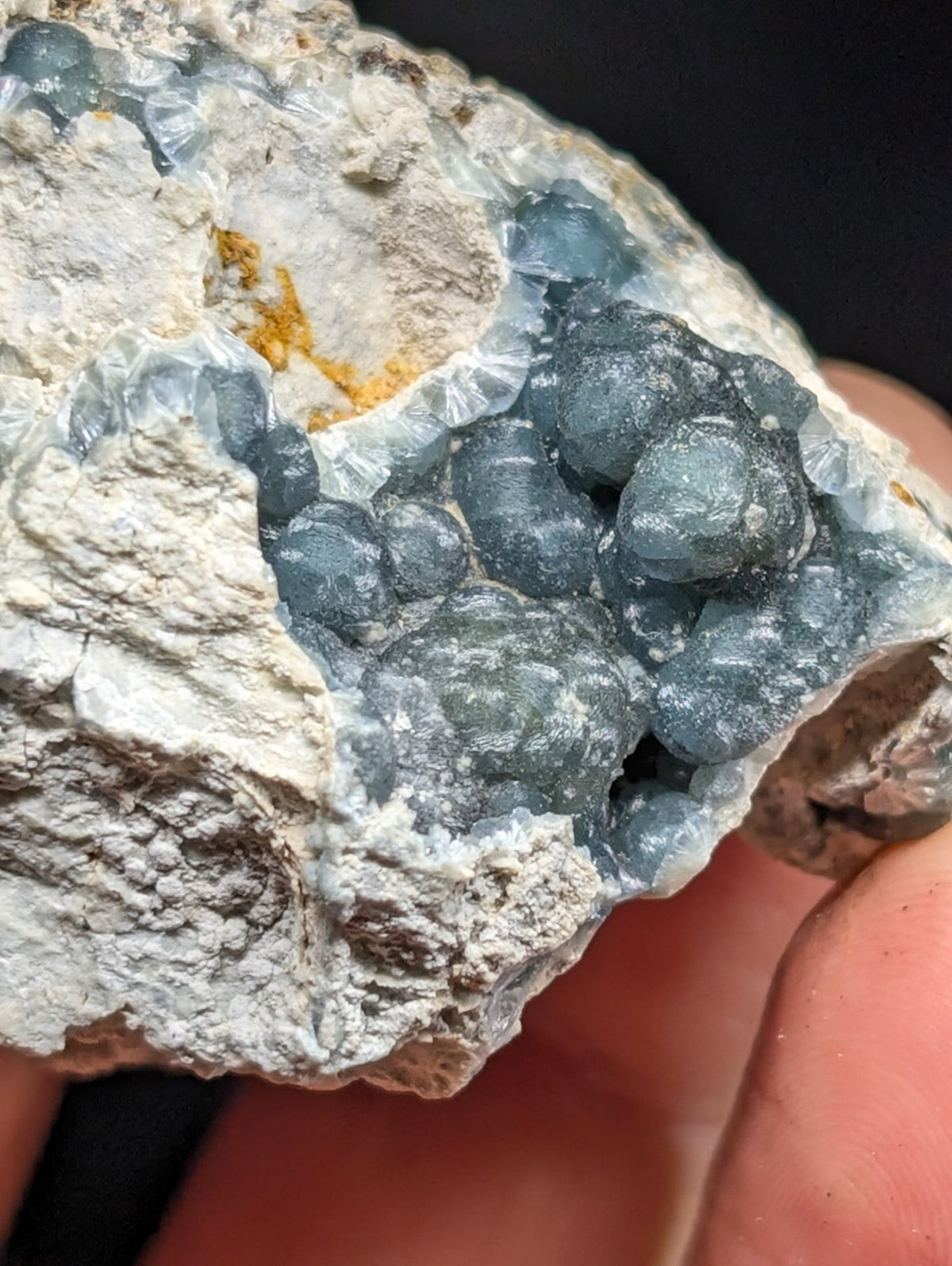 A cluster of translucent blue-gray crystals nestled within a rough, light gray rock matrix.
