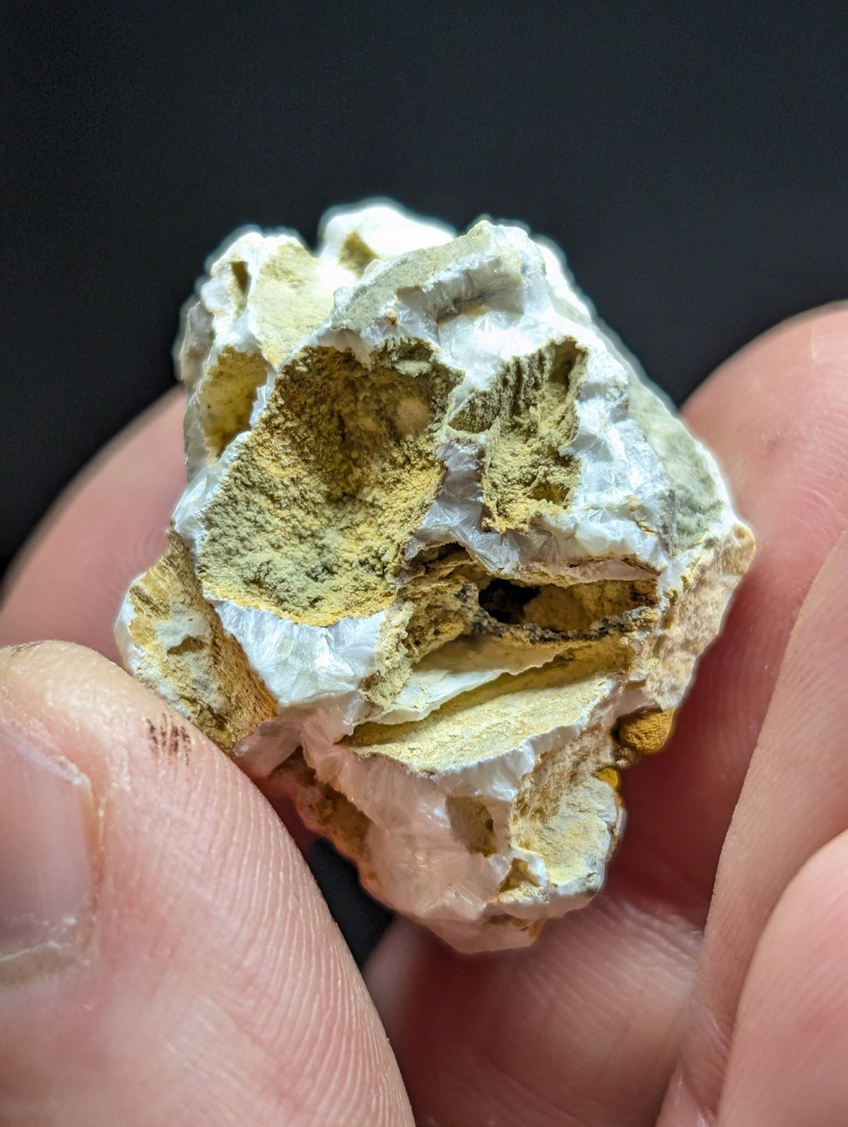 A rough, irregularly shaped mineral specimen with a white crystalline base and patches of yellowish-green material embedded within its surface.