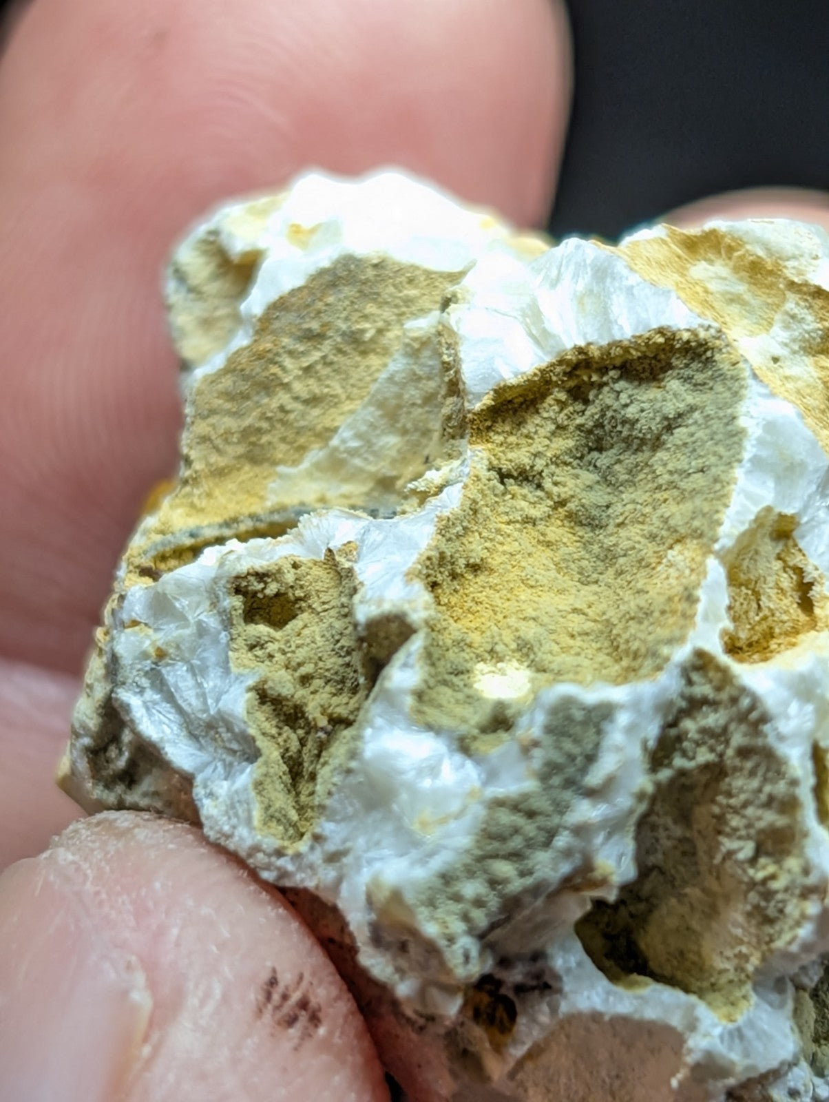 A textured mineral specimen with a white, porous matrix and patches of yellowish-green crystalline material.