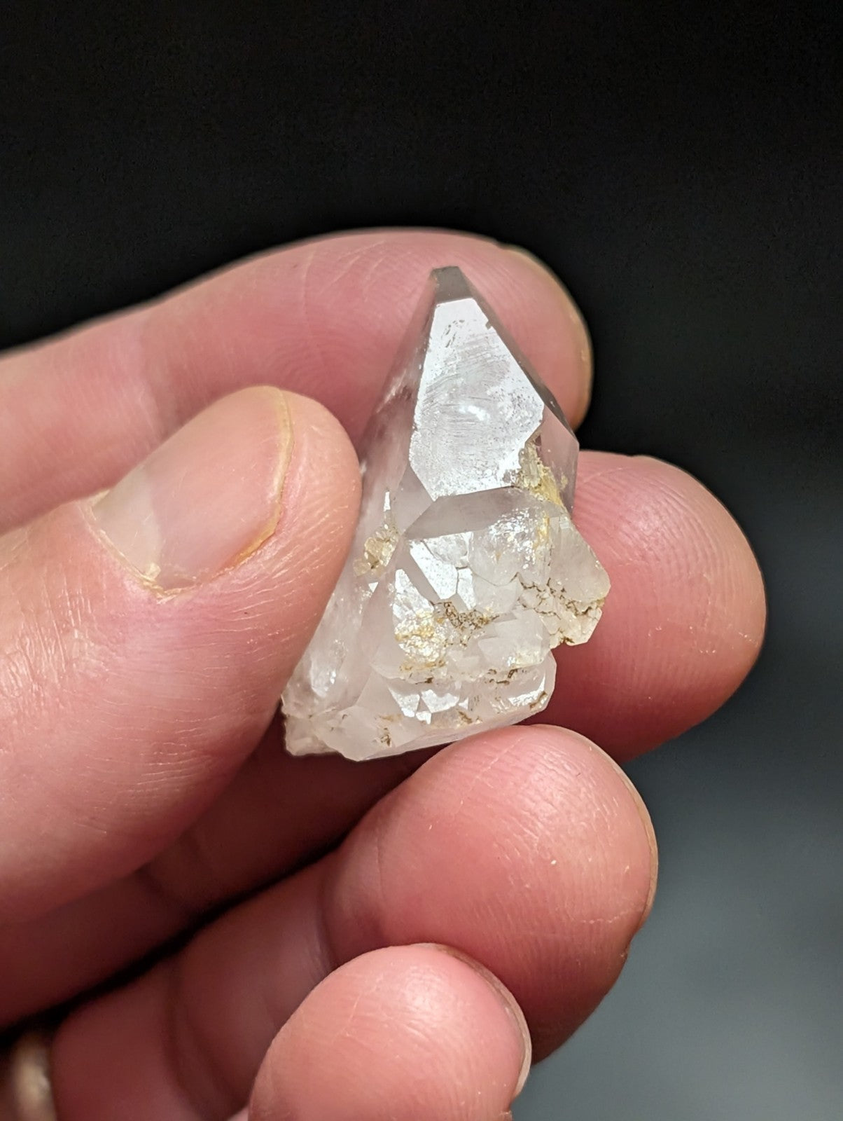 A clear, faceted quartz crystal with golden inclusions held gently between fingers.