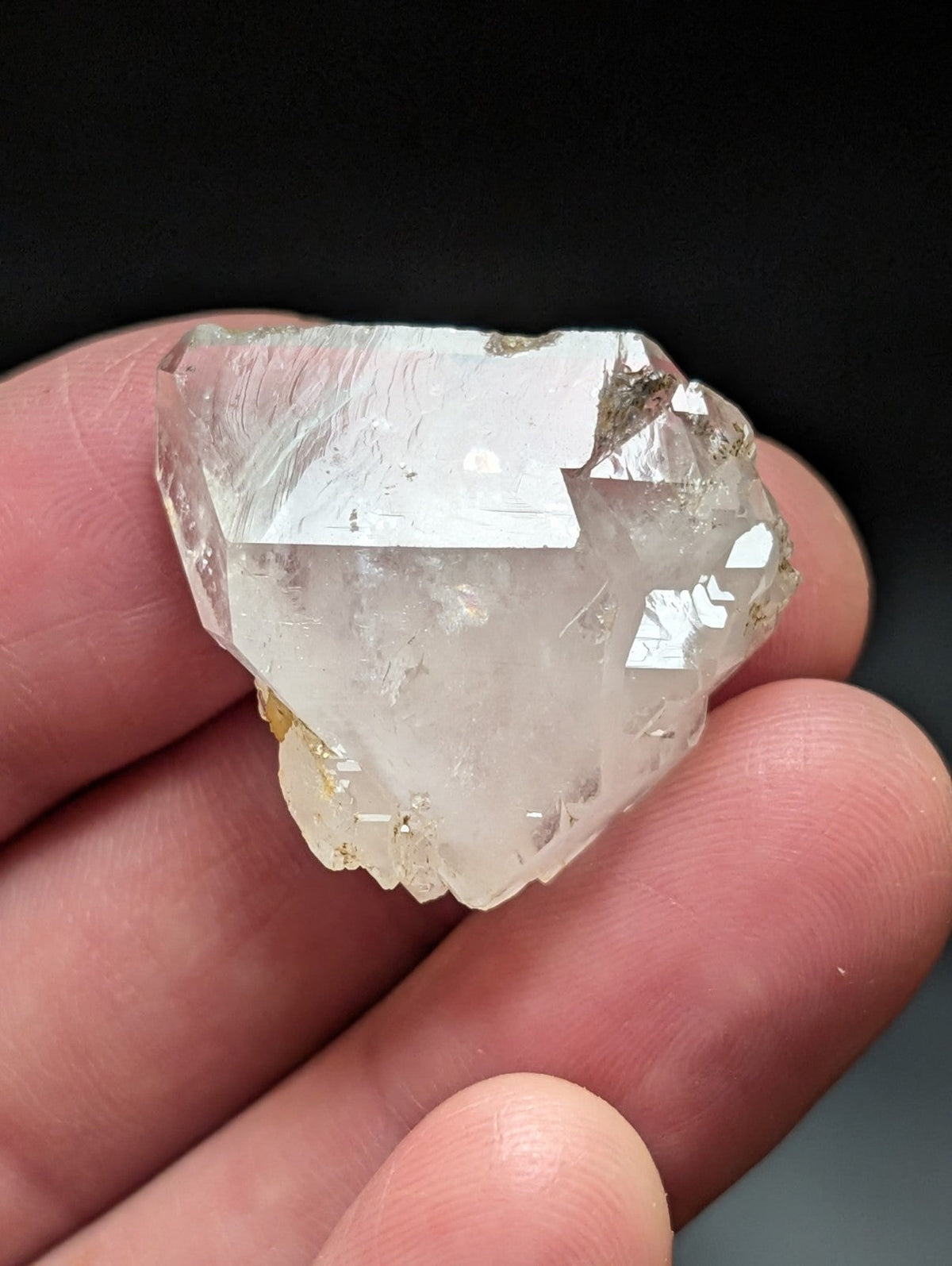 A translucent, clear quartz crystal with visible internal inclusions and a rough, natural surface held gently between fingers.