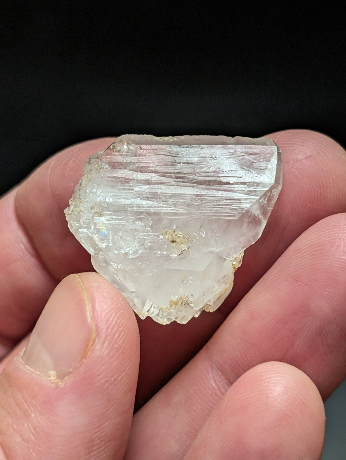 A translucent, pale greenish-white mineral specimen with visible striations and a rough, jagged surface.
