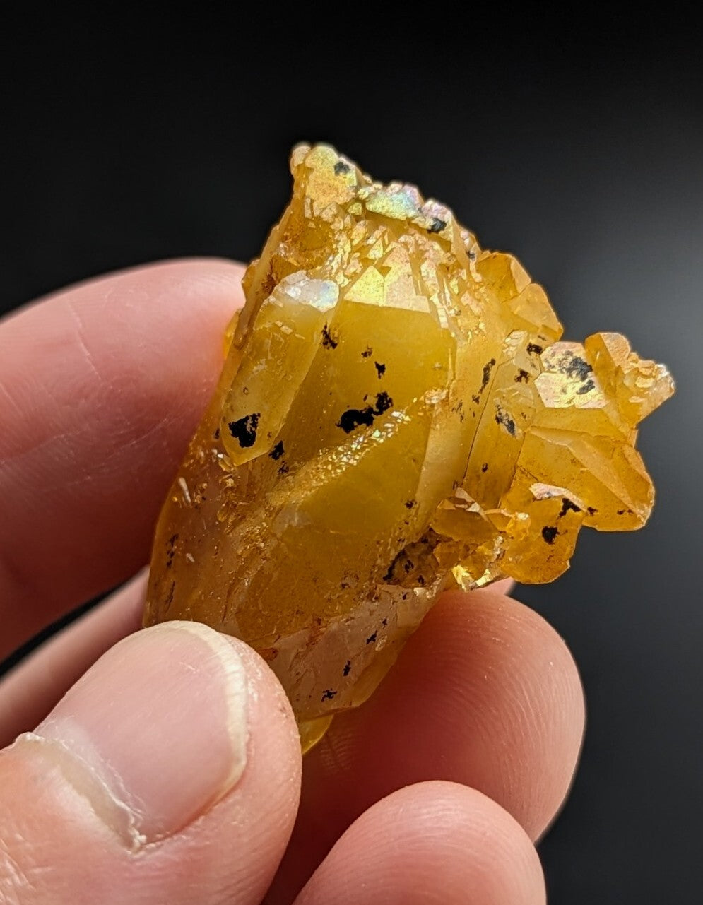 A translucent golden-yellow mineral specimen with crystalline facets and dark inclusions, held gently between fingers.