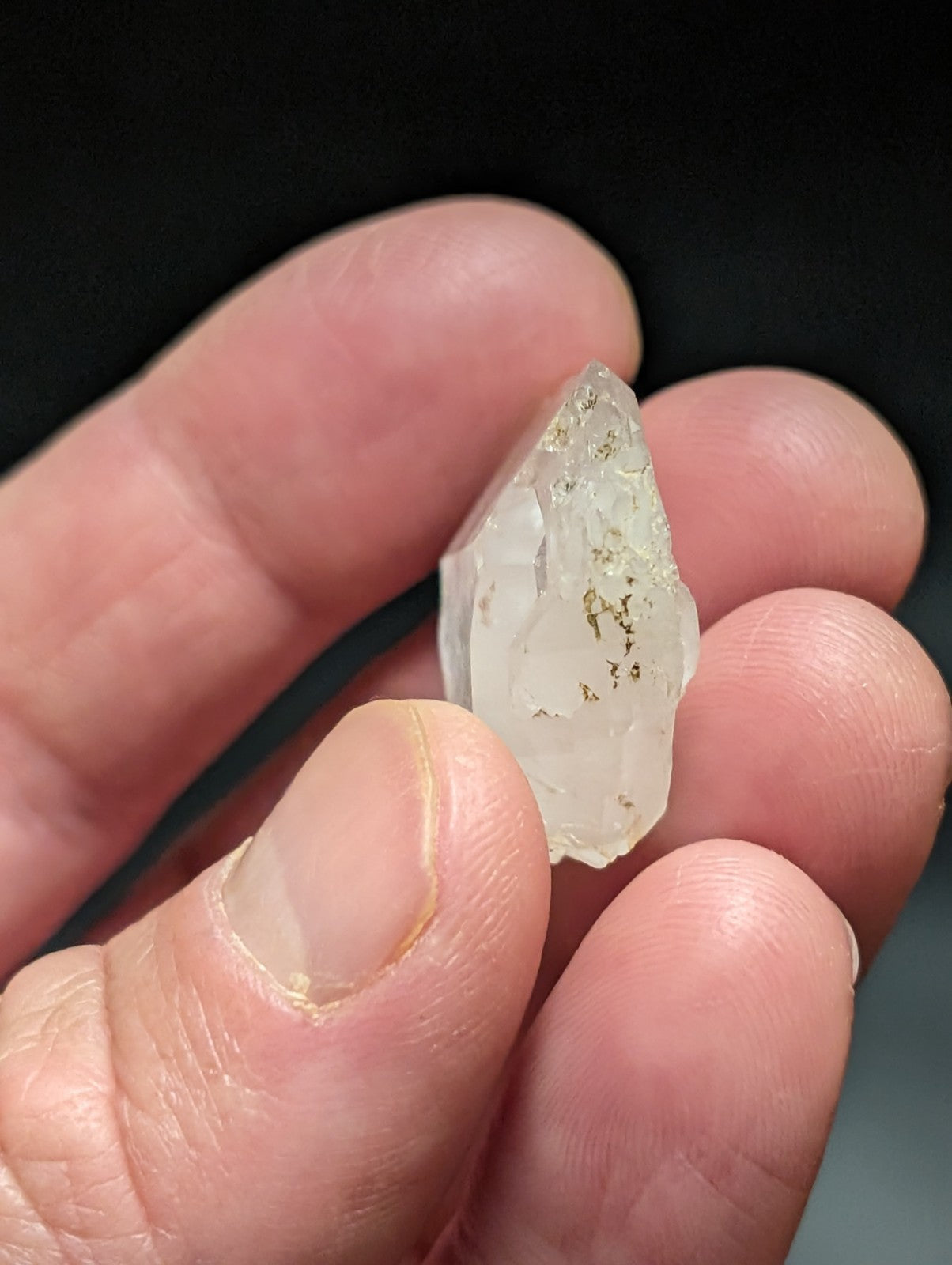 A translucent, pale quartz crystal with subtle golden inclusions and a pointed, faceted tip.