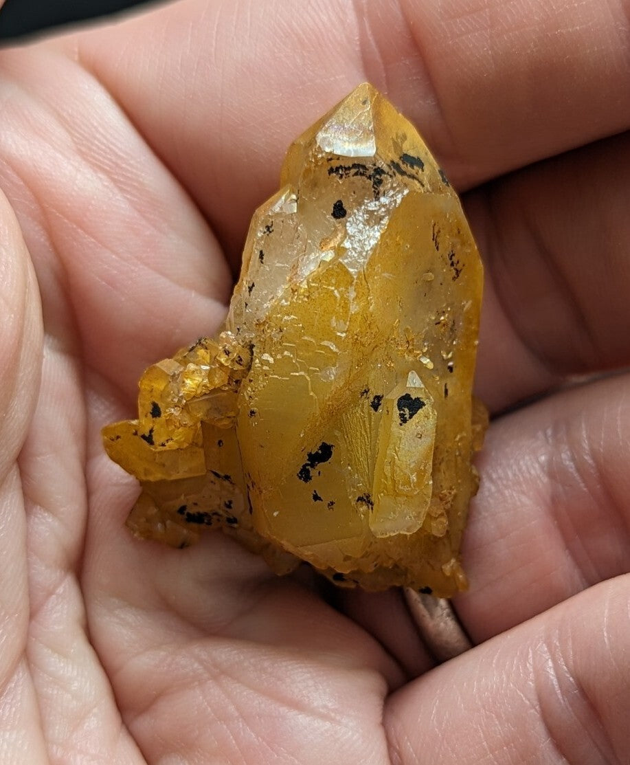 A translucent golden-yellow crystal cluster with dark inclusions, held gently in a person’s palm.