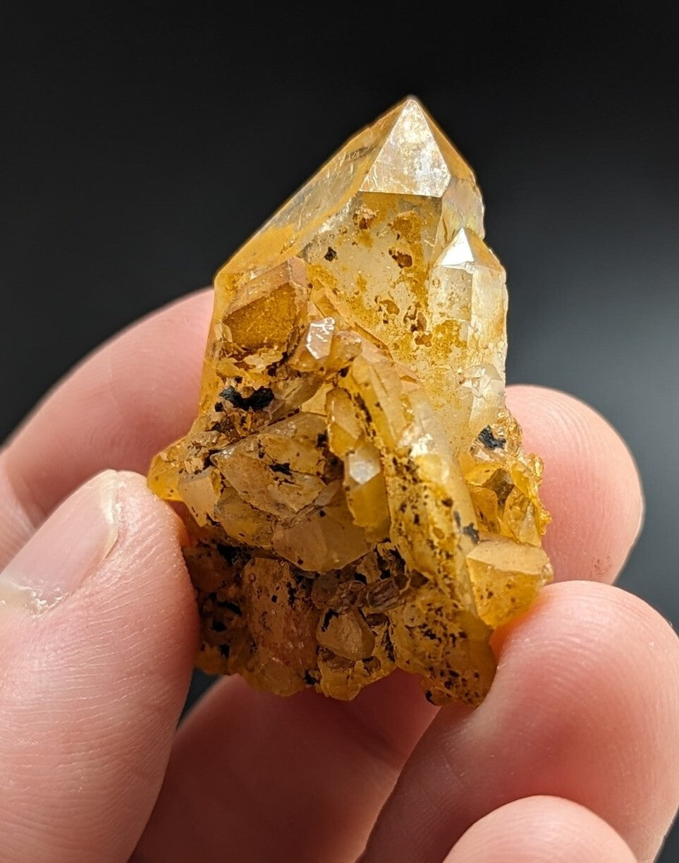 A translucent golden-yellow quartz crystal cluster with sharp, faceted points and embedded dark inclusions.