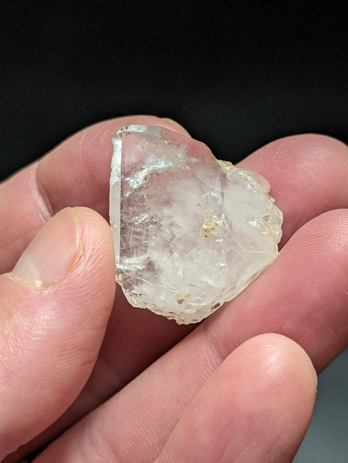 A translucent, irregularly shaped quartz crystal with subtle golden inclusions held gently between fingers.