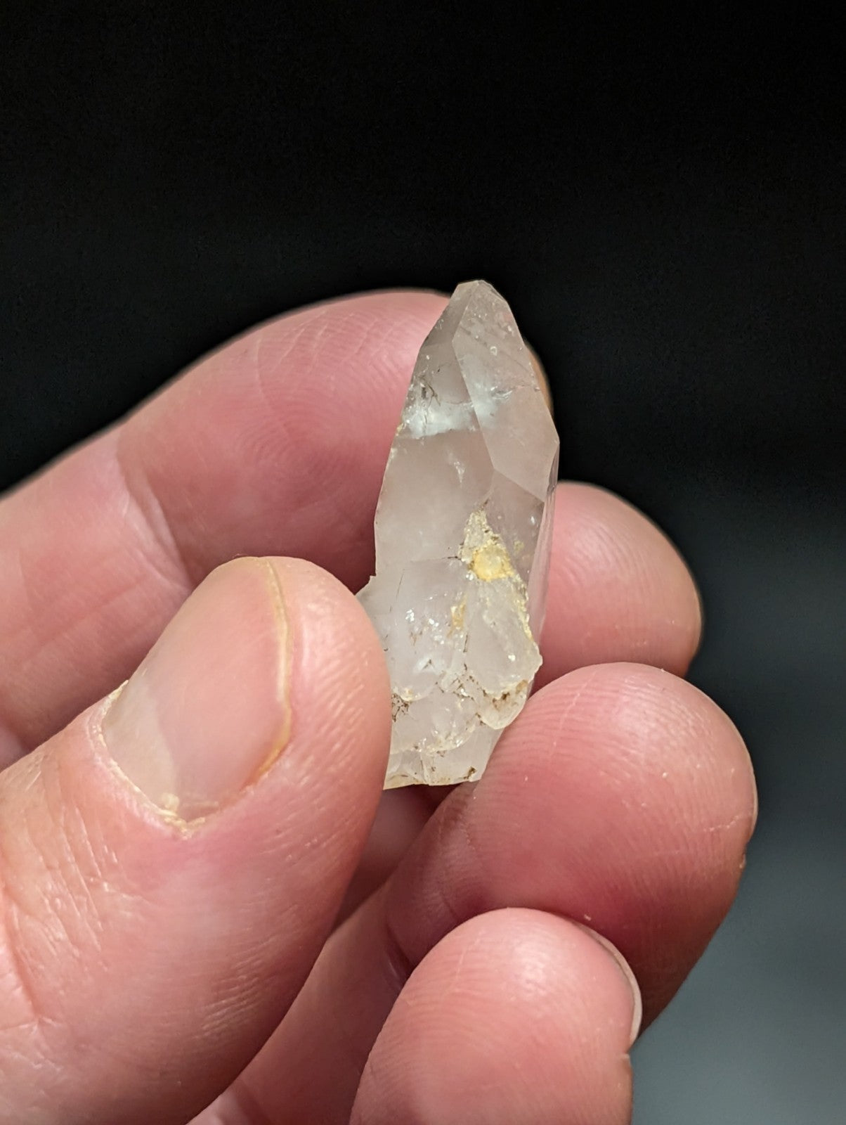 A translucent, pale quartz crystal with a pointed tip and subtle yellow inclusions.