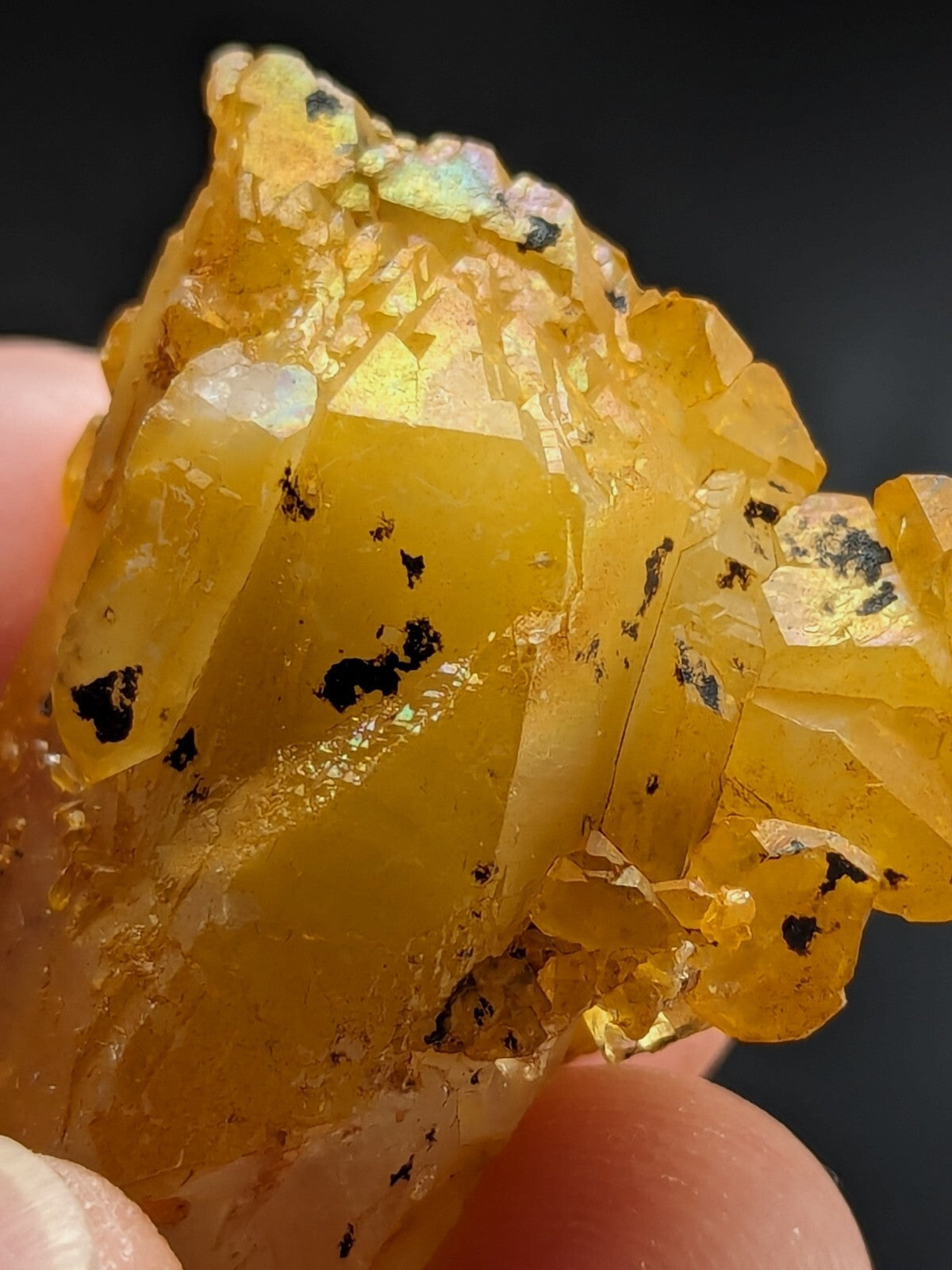 A translucent golden-yellow crystal cluster with iridescent facets and dark inclusions, held gently between fingers.