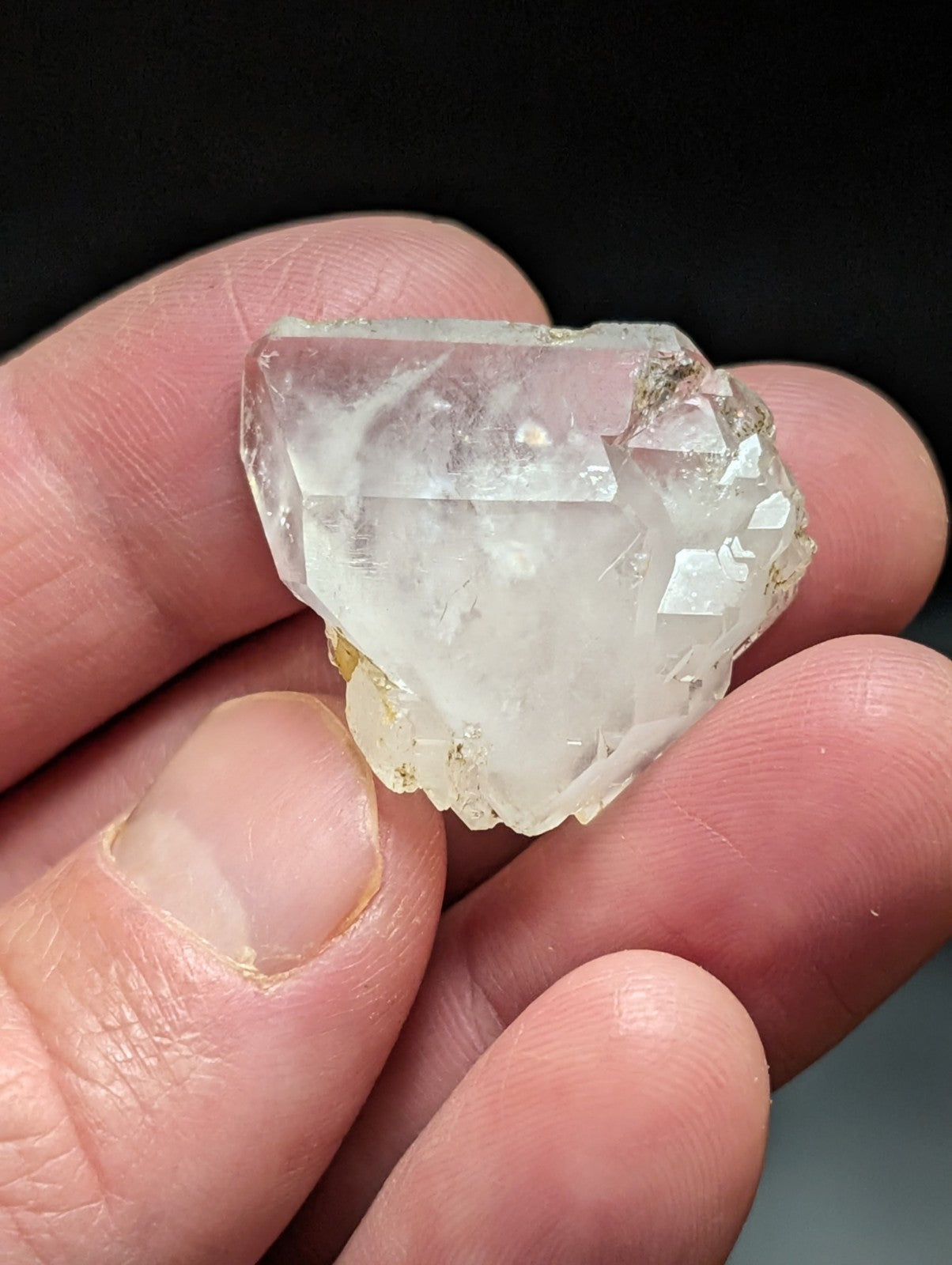 A translucent, faceted quartz crystal with a slightly cloudy interior and rough edges held in someone’s hand.