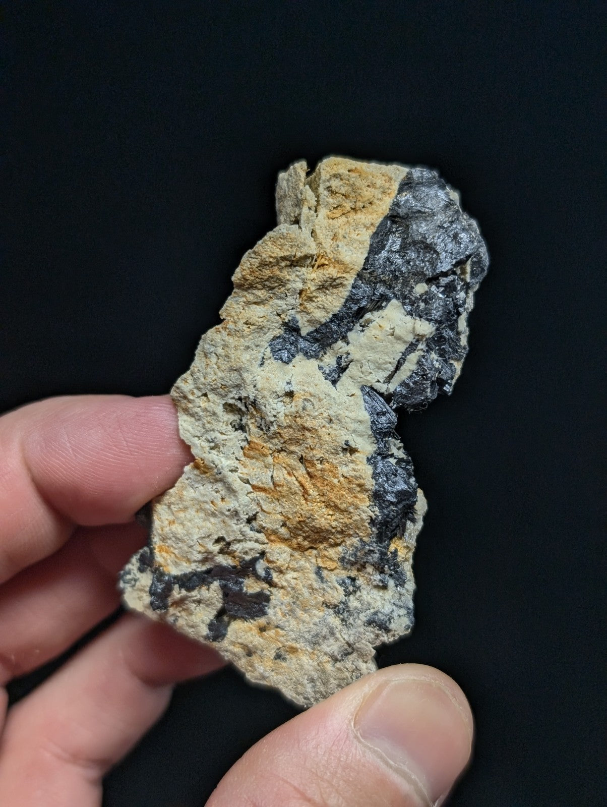 A rugged, irregularly shaped rock fragment with a mottled surface of beige, black, and orange hues.