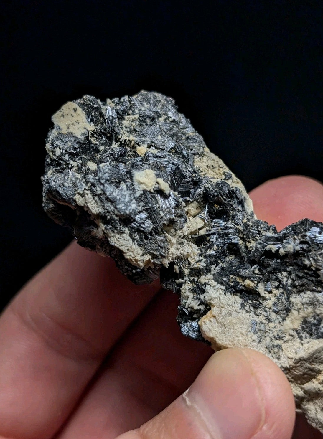 A rugged, naturally occurring mineral specimen with a dark gray and black matrix interspersed with lighter beige patches.