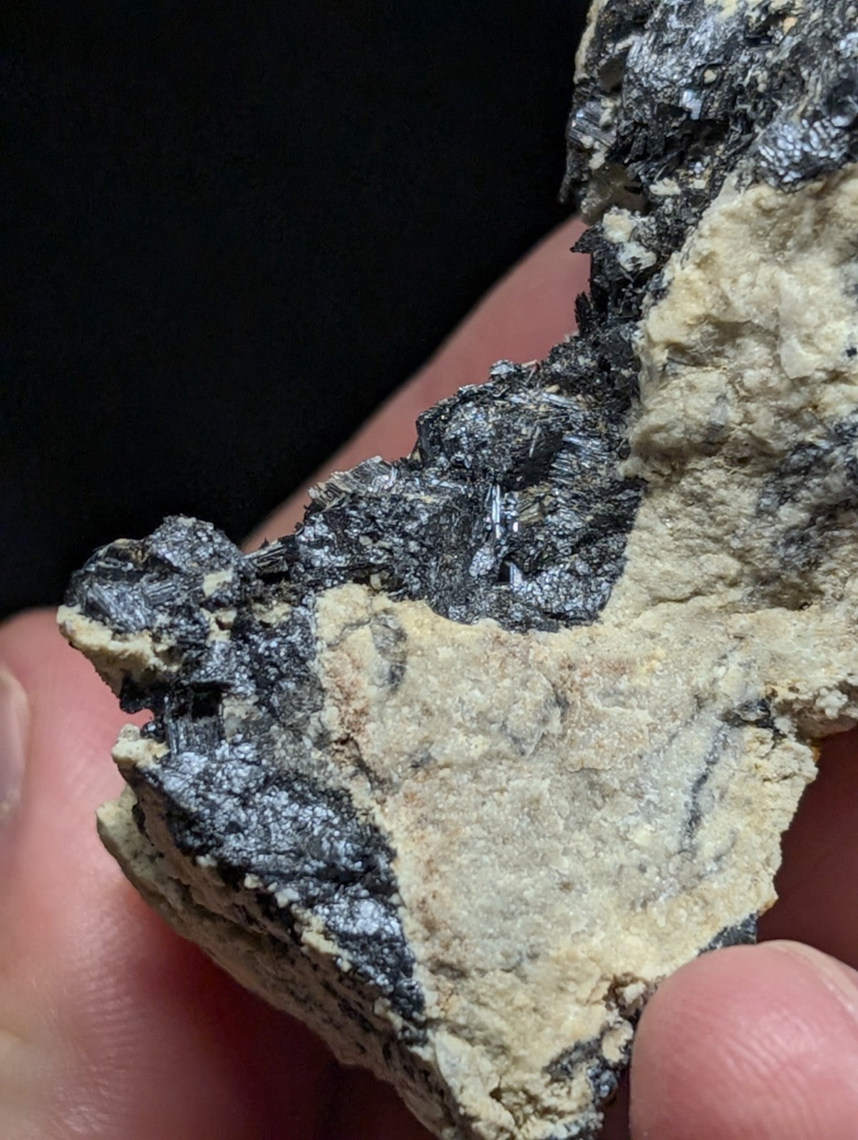 A rugged, irregularly shaped mineral specimen with a dark metallic sheen and patches of pale beige matrix.
