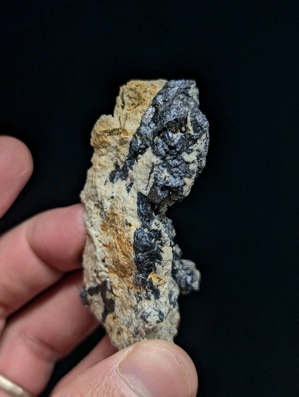 A rugged, irregularly shaped mineral specimen with a striking contrast of dark metallic veins against lighter beige and gray matrix.