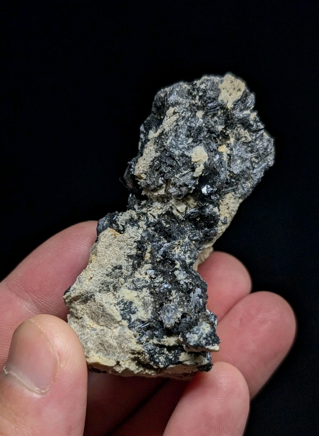 A rugged, irregularly shaped mineral specimen with a mottled black and gray surface accented by patches of pale yellowish-white.