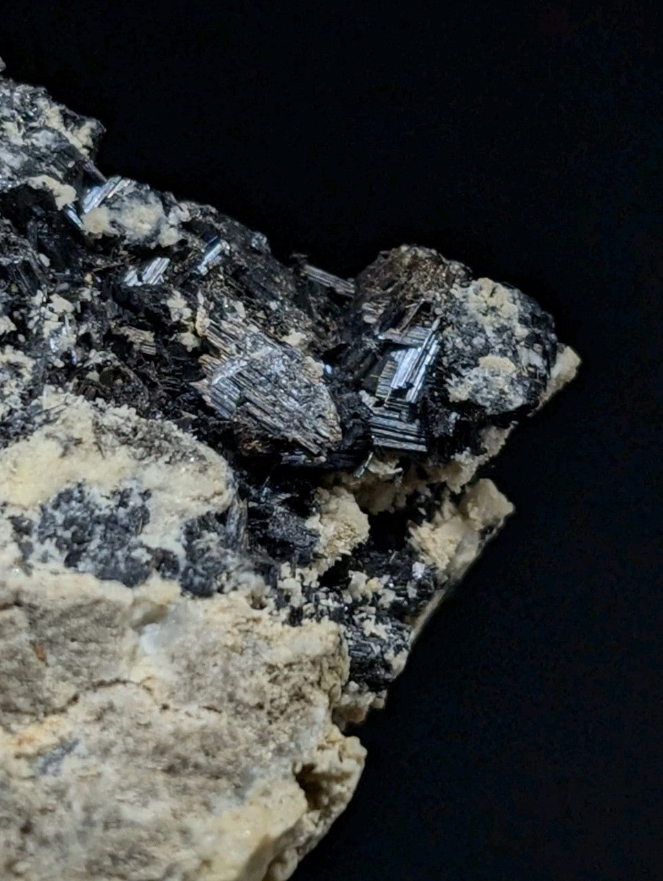 A cluster of dark, metallic-looking crystals with sharp edges and a slightly rough texture, embedded in a lighter-colored rock matrix.