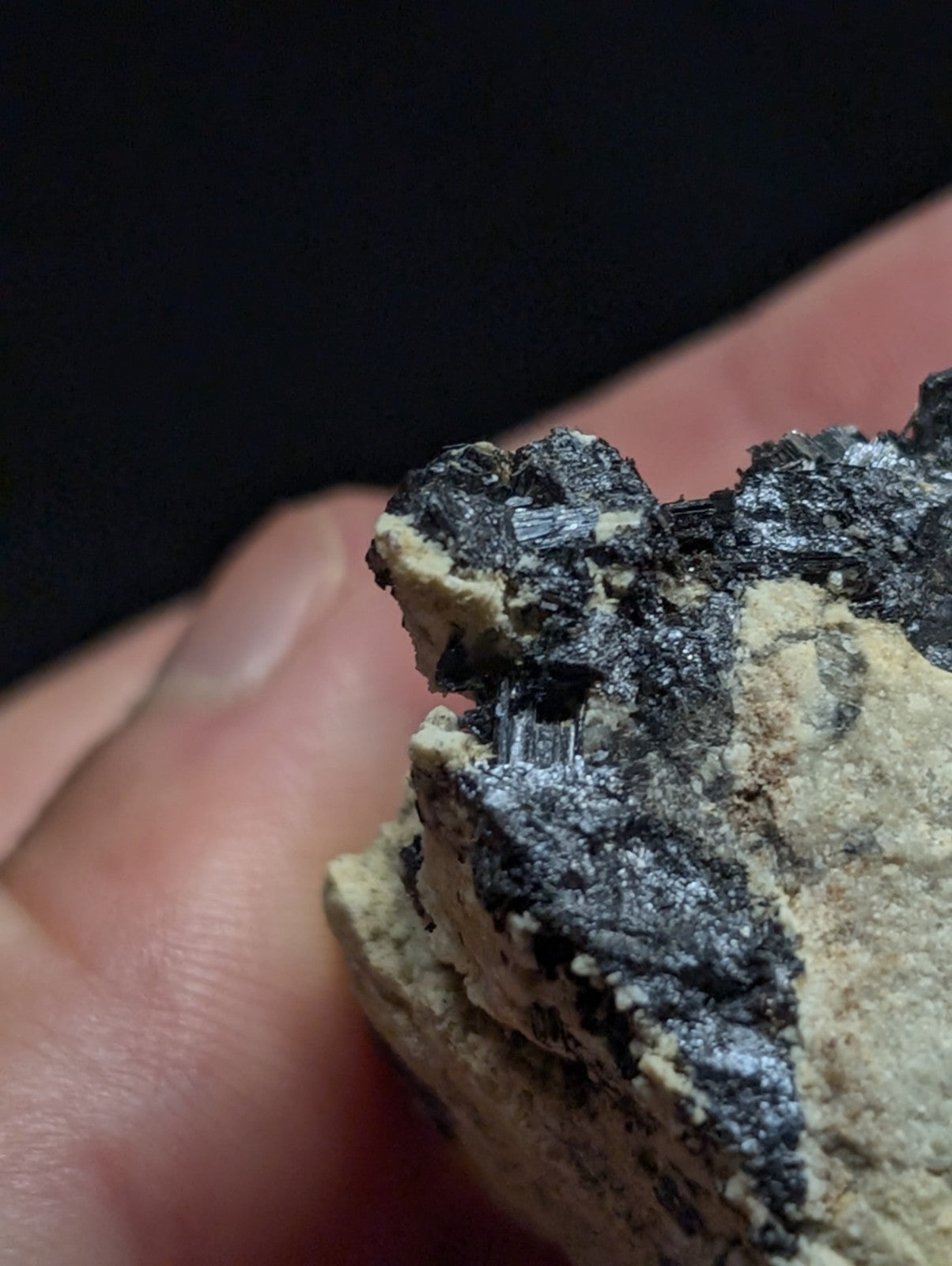 A hand holds a rough, irregularly shaped mineral specimen featuring dark black and gray crystalline formations embedded in a lighter beige matrix.