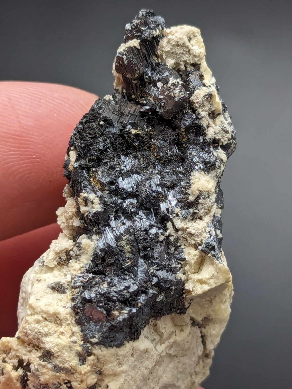 A dark, crystalline mineral specimen with metallic sheen embedded in a light beige matrix.