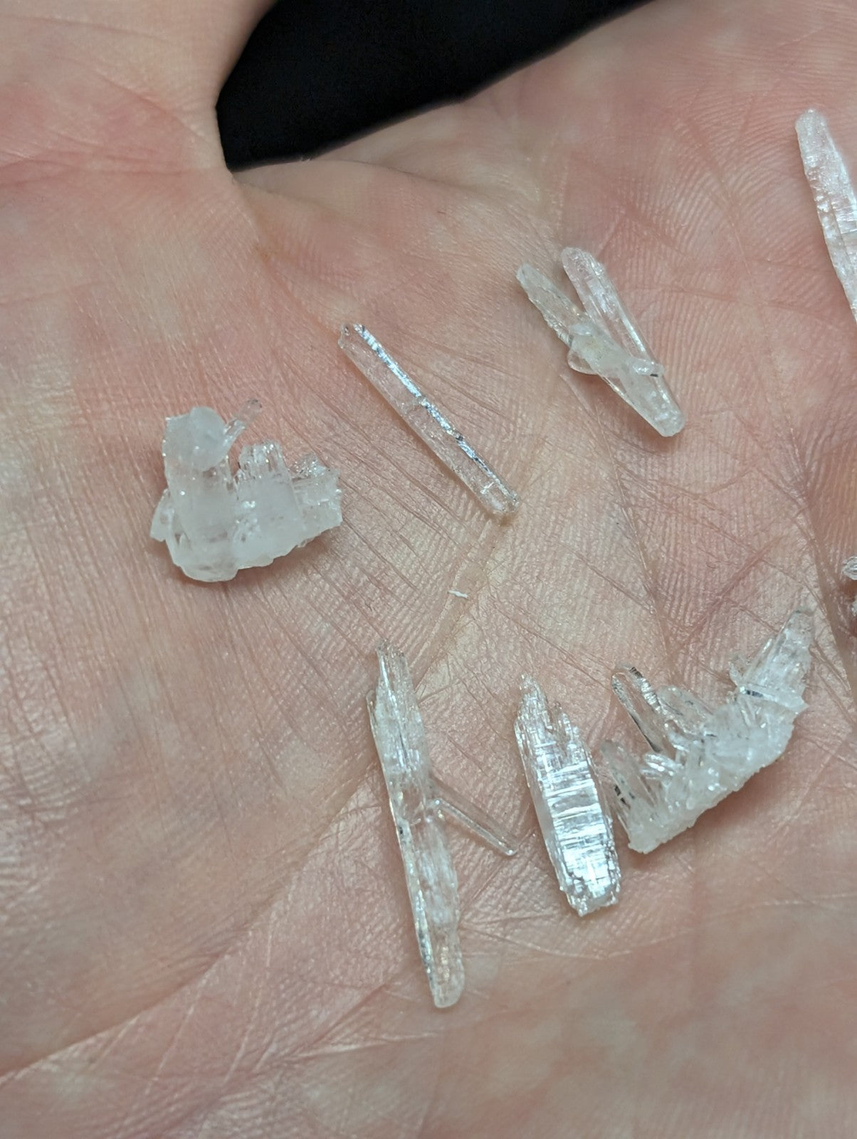 Clear, translucent quartz crystals with pointed tips and jagged edges rest in the palm.