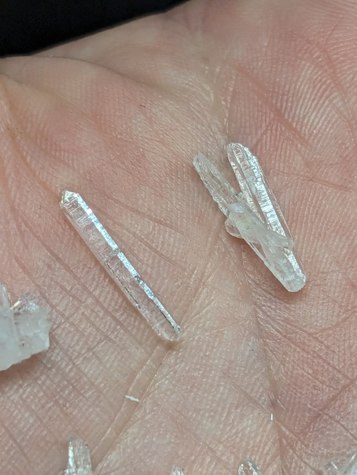 Clear quartz crystals with pointed tips and visible internal striations, resting in the palm of a hand.