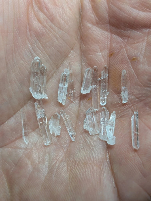 A collection of clear, translucent quartz crystals with jagged edges and varying lengths rests in an open palm.