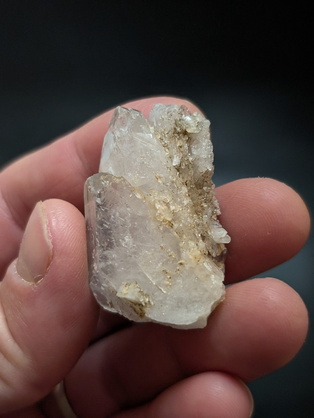 A translucent, clear quartz crystal with golden mineral inclusions held gently between fingers.