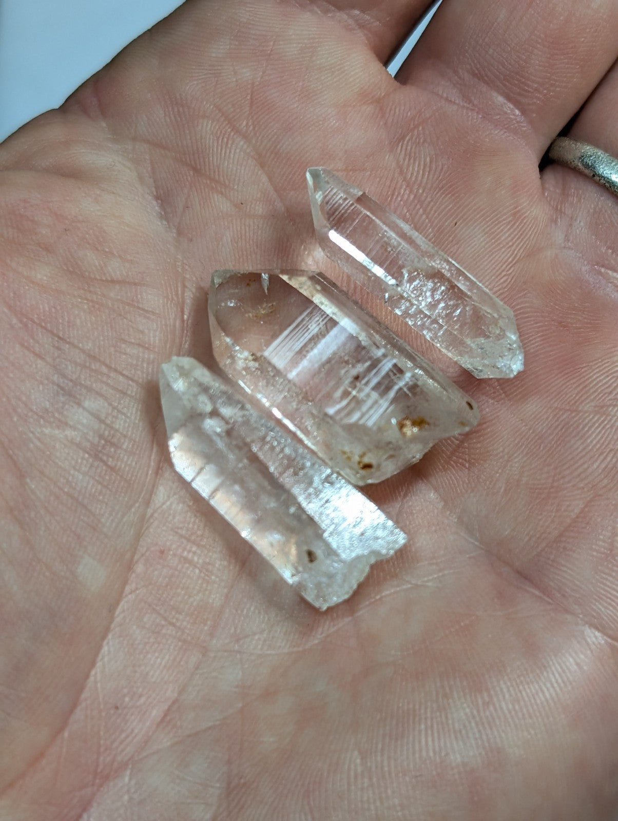Three clear quartz crystals with natural facets and subtle internal inclusions, held gently in an open palm.